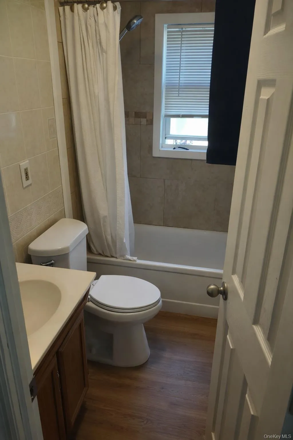 Full bathroom with dark wood-type flooring, vanity, shower / bath combo with shower curtain, and tile walls Full bathroom with dark wood-type flooring, vanity, shower / bath combo with shower curtain, and tile walls