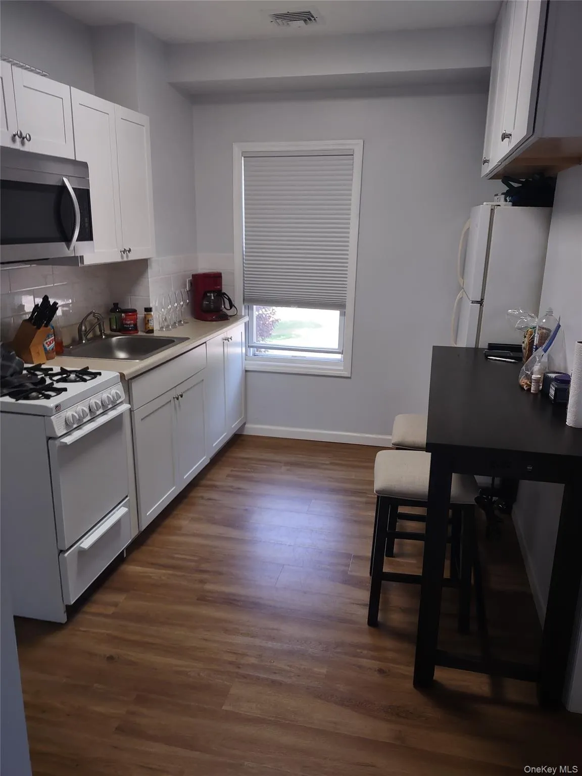 Kitchen with white appliances, white cabinets, light countertops, dark wood-style floors, and tasteful backsplash Kitchen with white appliances, white cabinets, light countertops, dark wood-style floors, and tasteful backsplash