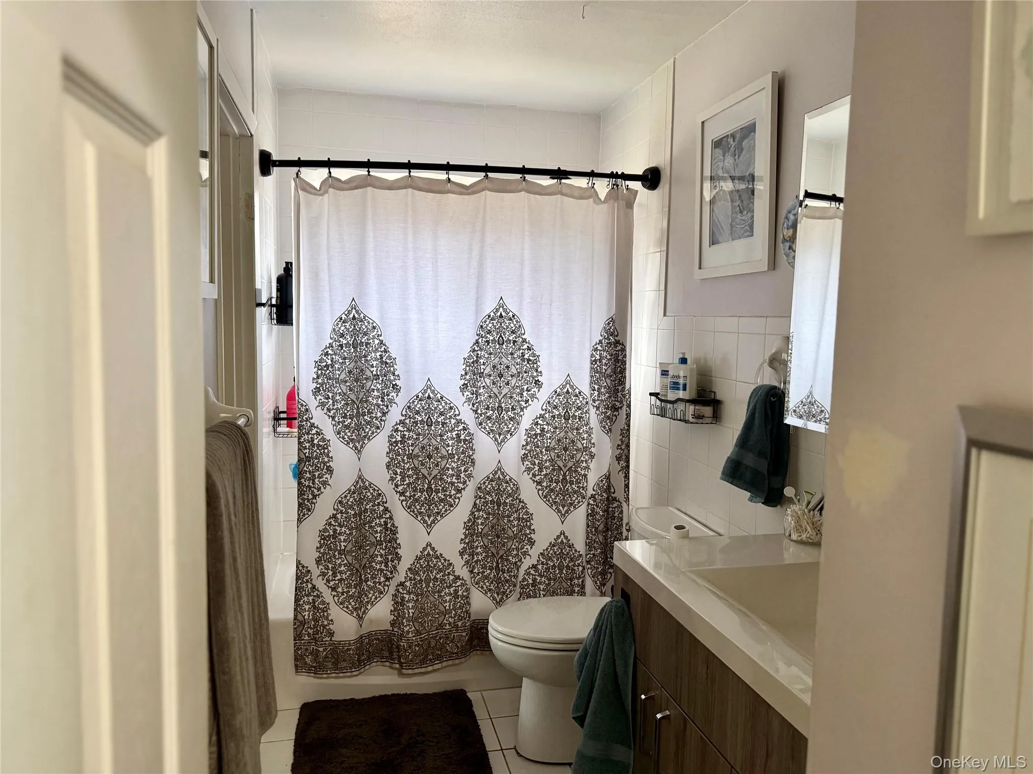 Full bath featuring vanity, shower / bath combination with curtain, light tile patterned flooring, and tile walls Full bath featuring vanity, shower / bath combination with curtain, light tile patterned flooring, and tile walls