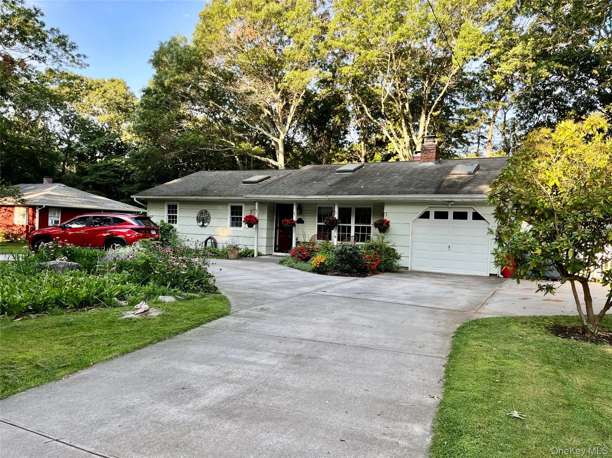 Ranch-style home with concrete driveway, a chimney, an attached garage, and view of wooded area Ranch-style home with concrete driveway, a chimney, an attached garage, and view of wooded area