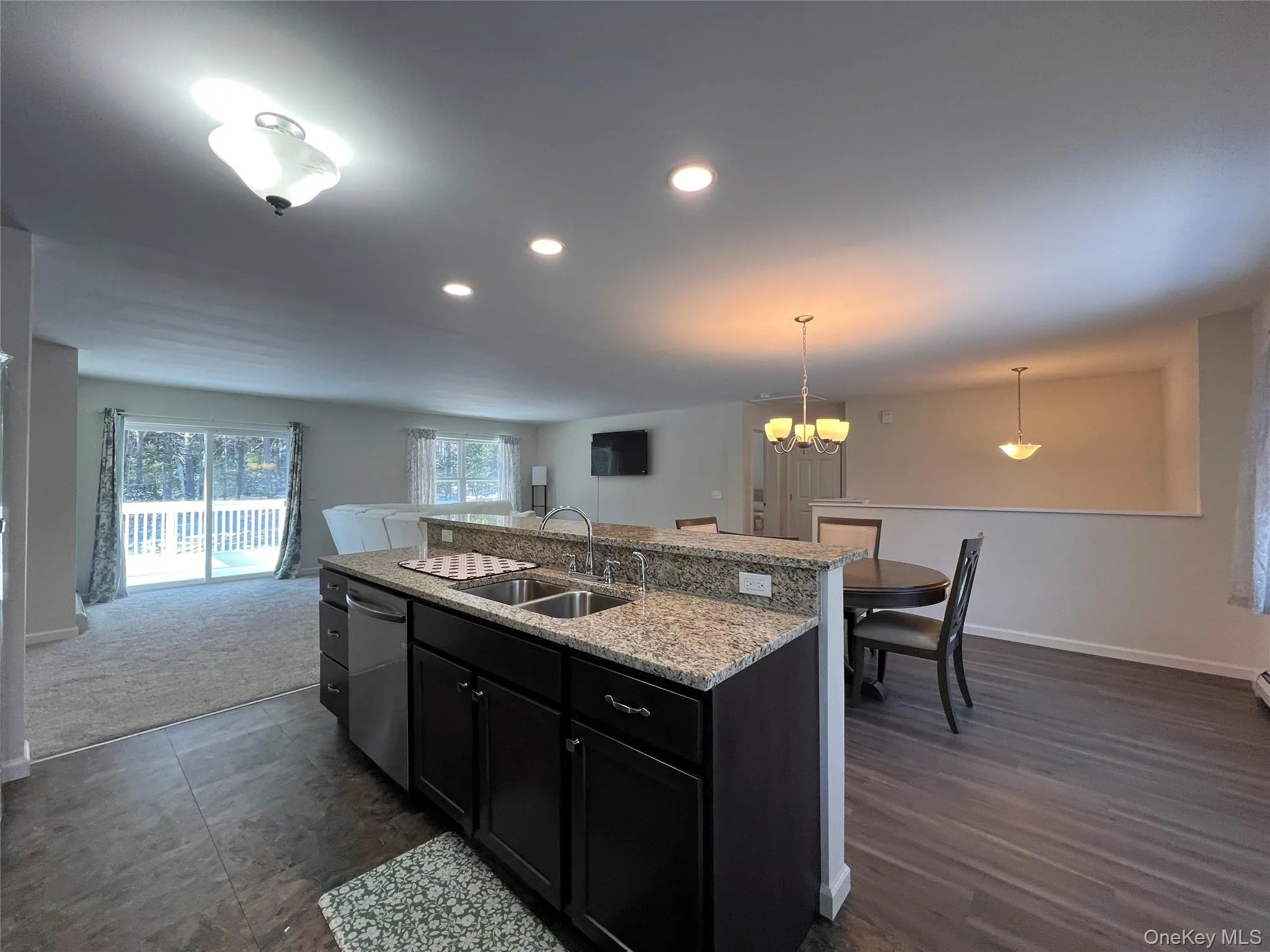 Kitchen with dark cabinetry, a kitchen island with sink, light stone countertops, decorative light fixtures, and dishwasher Kitchen with dark cabinetry, a kitchen island with sink, light stone countertops, decorative light fixtures, and dishwasher