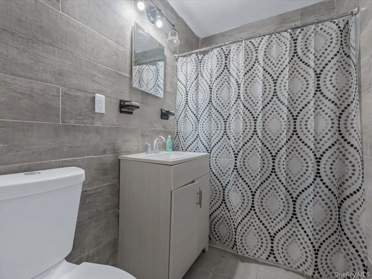 Bathroom with vanity, a shower with shower curtain, light tile patterned floors, and tile walls Bathroom with vanity, a shower with shower curtain, light tile patterned floors, and tile walls