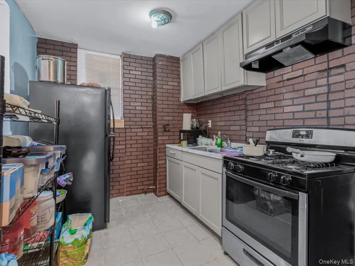 Kitchen with stainless steel range with gas cooktop, brick wall, under cabinet range hood, freestanding refrigerator, and light tile patterned floors Kitchen with stainless steel range with gas cooktop, brick wall, under cabinet range hood, freestanding refrigerator, and light tile patterned floors