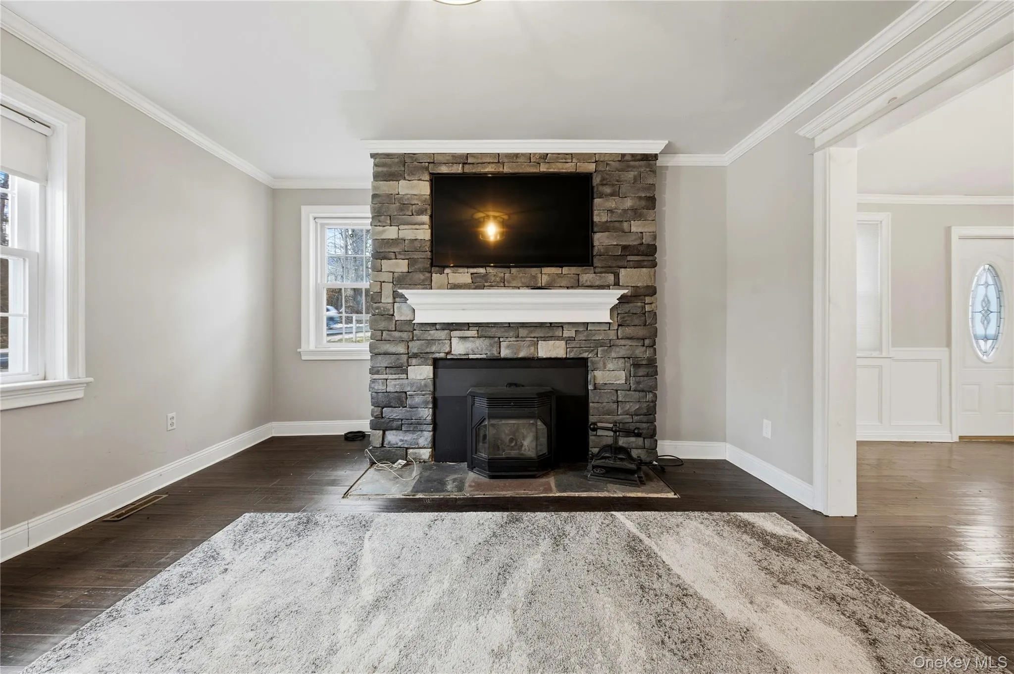 Unfurnished living room featuring dark wood-style floors and ornamental molding Unfurnished living room featuring dark wood-style floors and ornamental molding