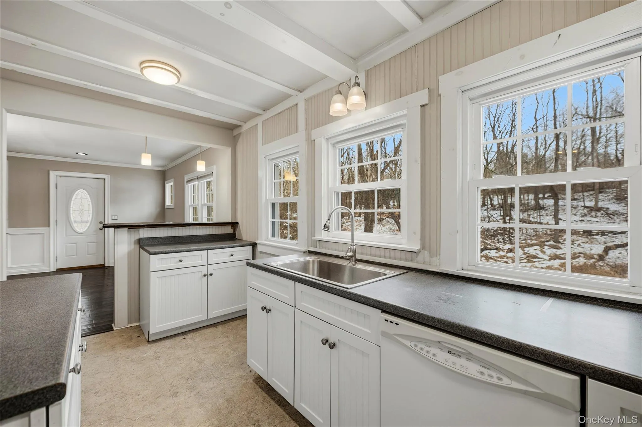 Kitchen featuring white cabinets, dark countertops, white dishwasher, pendant lighting, and a decorative wall Kitchen featuring white cabinets, dark countertops, white dishwasher, pendant lighting, and a decorative wall