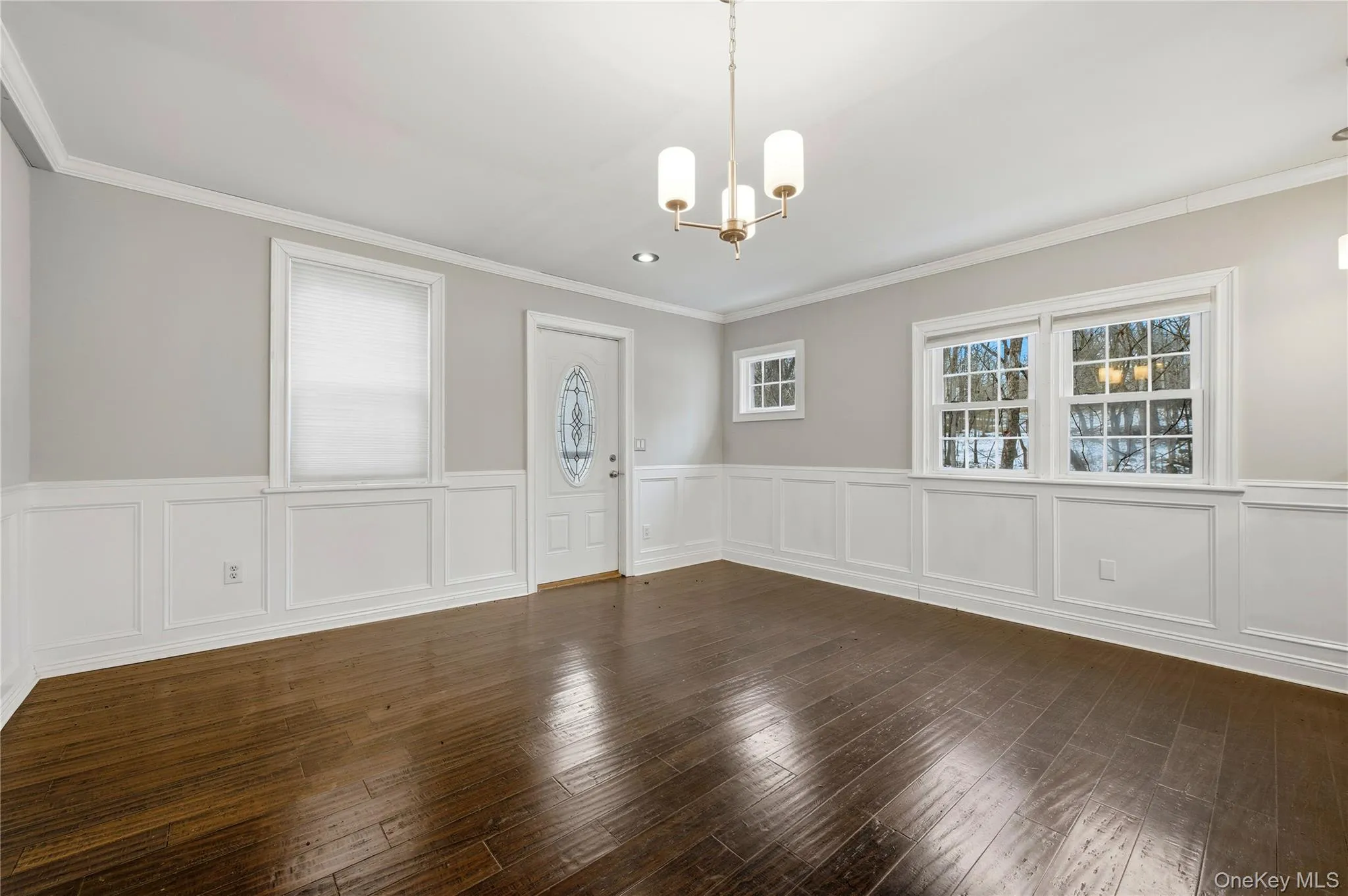 Unfurnished dining area featuring plenty of natural light, a chandelier, dark wood-type flooring, ornamental molding, and a wainscoted wall Unfurnished dining area featuring plenty of natural light, a chandelier, dark wood-type flooring, ornamental molding, and a wainscoted wall