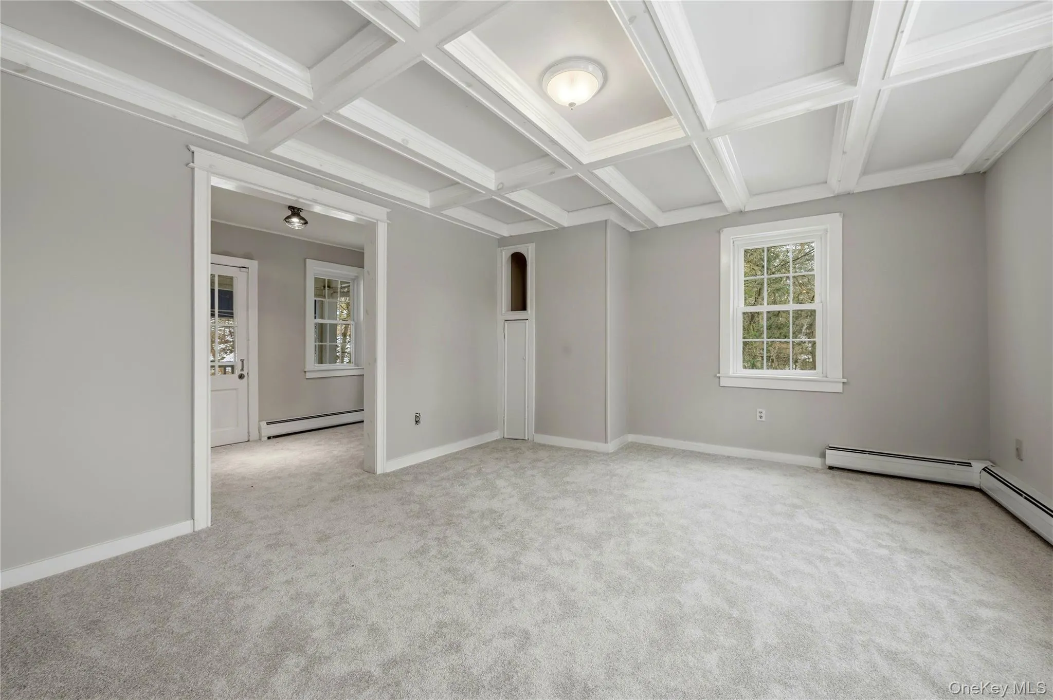 Unfurnished room featuring coffered ceiling, beam ceiling, a baseboard radiator, light carpet, and crown molding Unfurnished room featuring coffered ceiling, beam ceiling, a baseboard radiator, light carpet, and crown molding