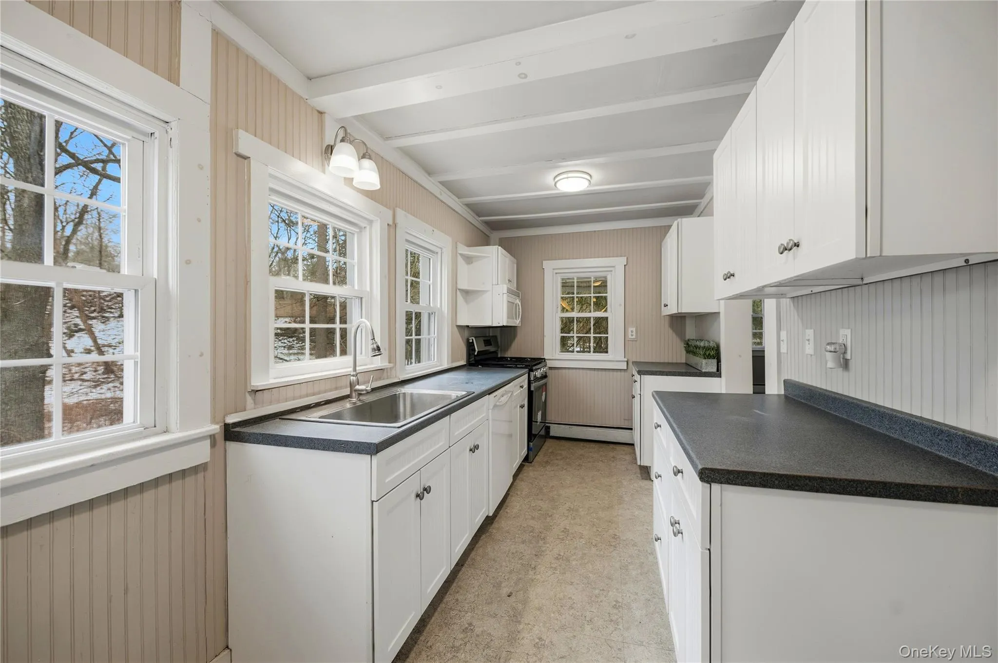 Kitchen with wooden walls, dark countertops, white cabinets, stainless steel gas range, and white dishwasher Kitchen with wooden walls, dark countertops, white cabinets, stainless steel gas range, and white dishwasher