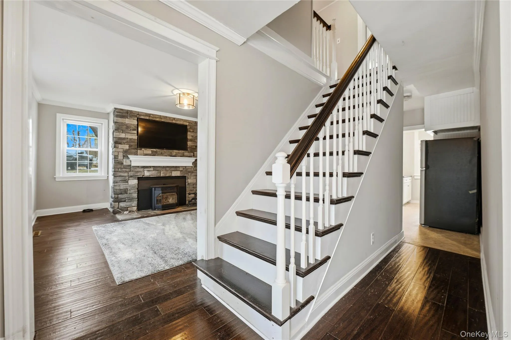 Staircase with wood-type flooring, crown molding, and a stone fireplace Staircase with wood-type flooring, crown molding, and a stone fireplace