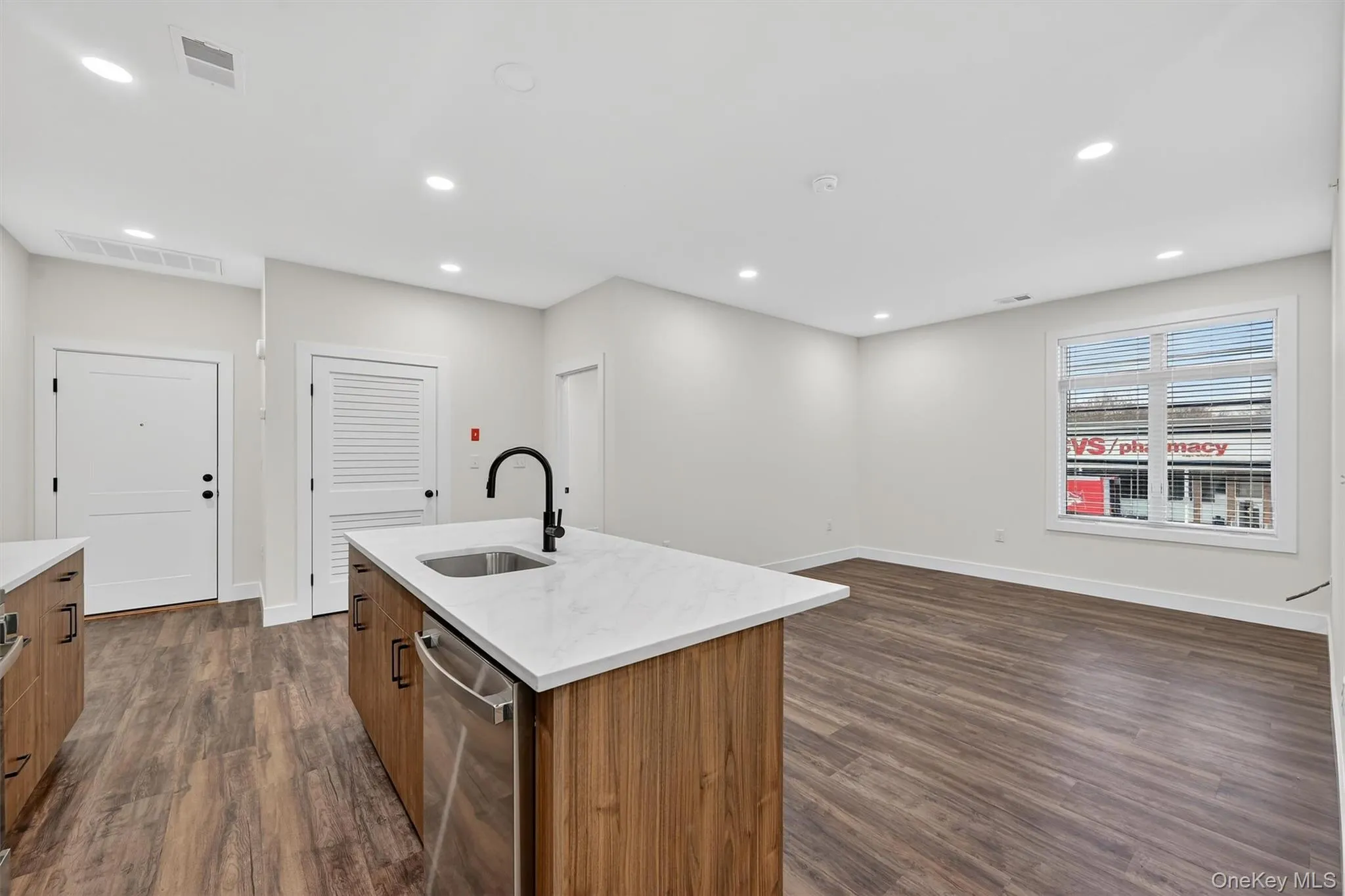 Kitchen with brown cabinetry, dark wood-style flooring, light stone countertops, dishwasher, and recessed lighting Kitchen with brown cabinetry, dark wood-style flooring, light stone countertops, dishwasher, and recessed lighting