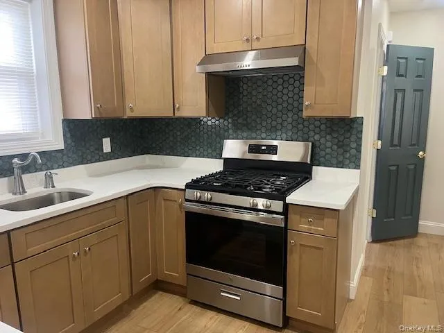 Kitchen with stainless steel range with gas cooktop, under cabinet range hood, backsplash, and light wood-type flooring Kitchen with stainless steel range with gas cooktop, under cabinet range hood, backsplash, and light wood-type flooring