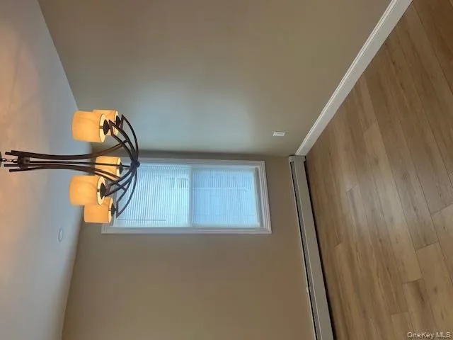 Empty room with baseboard heating, light wood-style floors, and a chandelier Empty room with baseboard heating, light wood-style floors, and a chandelier