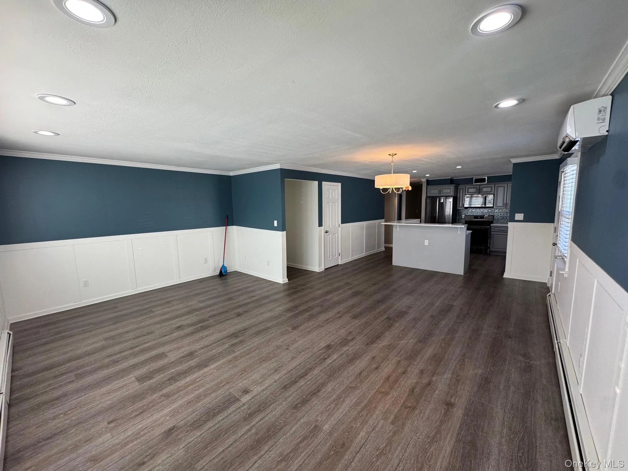 Unfurnished living room with a wainscoted wall, recessed lighting, a decorative wall, a baseboard radiator, and dark wood finished floors Unfurnished living room with a wainscoted wall, recessed lighting, a decorative wall, a baseboard radiator, and dark wood finished floors