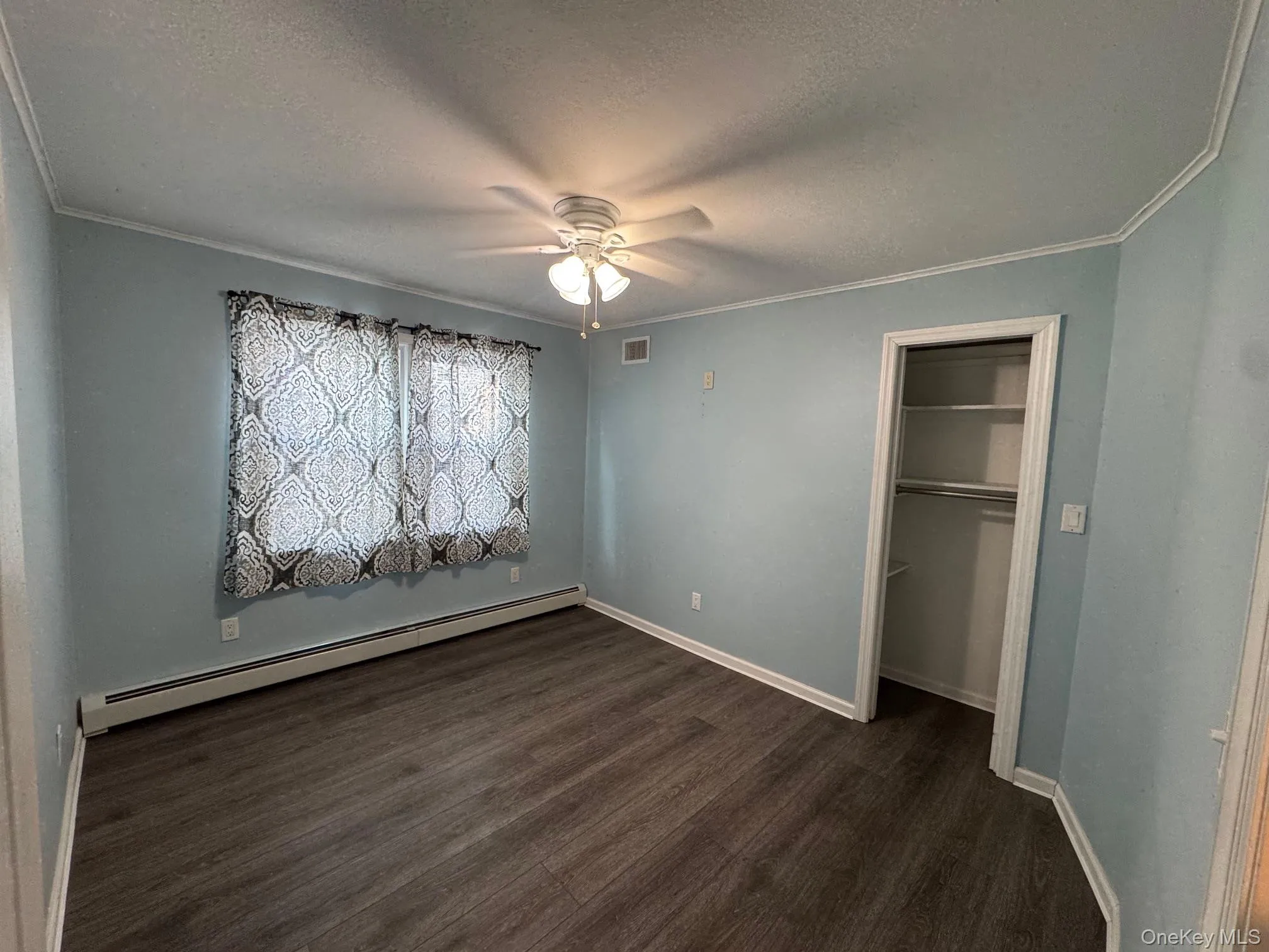 Unfurnished bedroom with a baseboard radiator, a textured ceiling, a closet, dark wood-style floors, and ceiling fan Unfurnished bedroom with a baseboard radiator, a textured ceiling, a closet, dark wood-style floors, and ceiling fan
