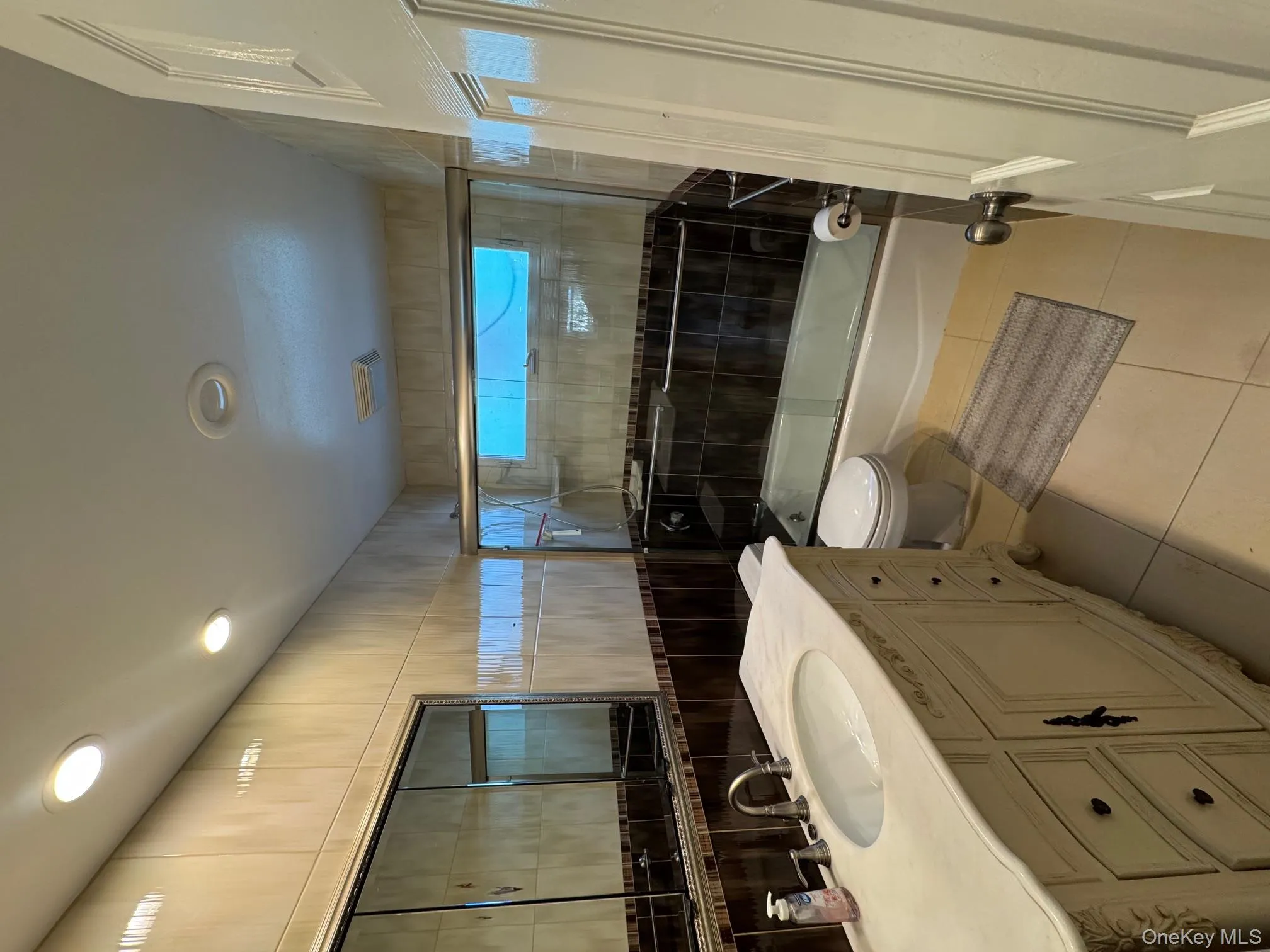 Bathroom with light tile patterned floors, vanity, tile walls, bath / shower combo with glass door, and recessed lighting Bathroom with light tile patterned floors, vanity, tile walls, bath / shower combo with glass door, and recessed lighting