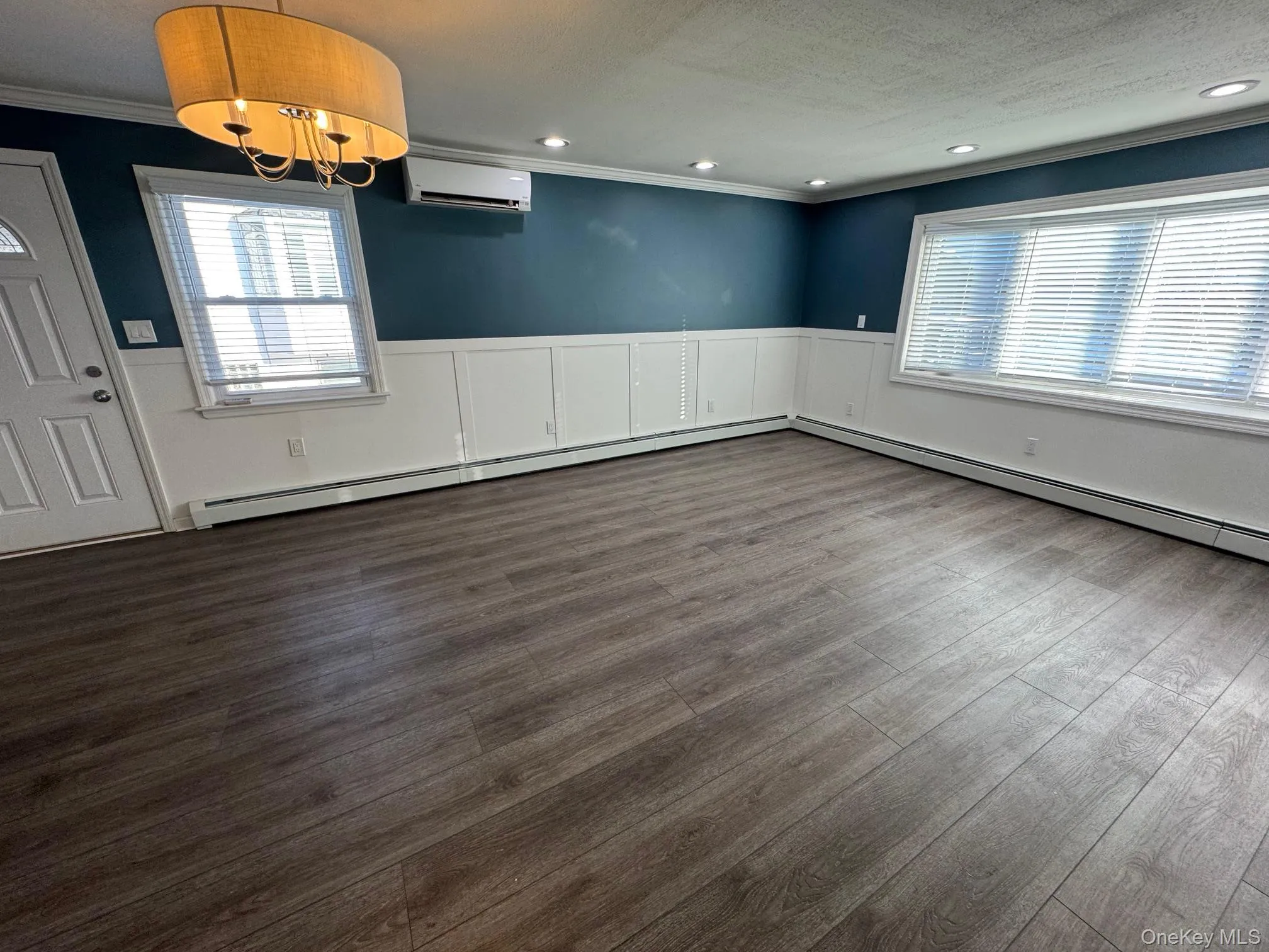 Unfurnished dining area with a baseboard radiator, a wainscoted wall, a textured ceiling, crown molding, and a chandelier Unfurnished dining area with a baseboard radiator, a wainscoted wall, a textured ceiling, crown molding, and a chandelier