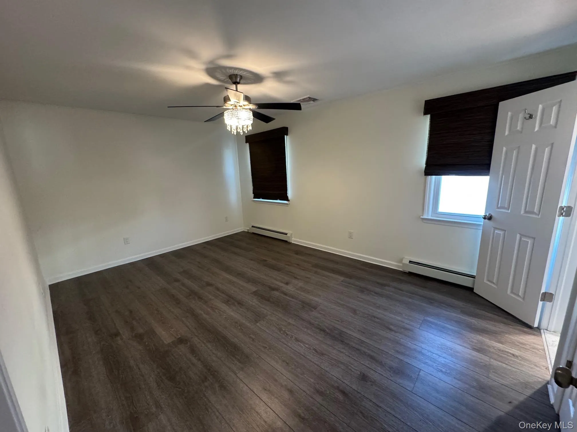 Spare room featuring a baseboard heating unit, dark wood-style flooring, and a ceiling fan Spare room featuring a baseboard heating unit, dark wood-style flooring, and a ceiling fan