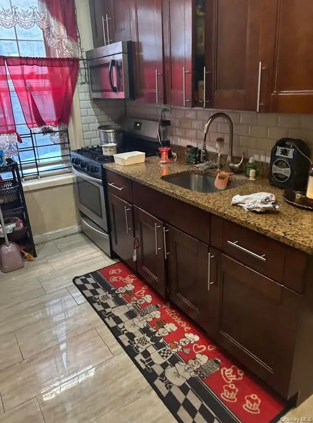 Kitchen with dark stone counters, stainless steel appliances, wood finish floors, tasteful backsplash, and dark brown cabinetry Kitchen with dark stone counters, stainless steel appliances, wood finish floors, tasteful backsplash, and dark brown cabinetry