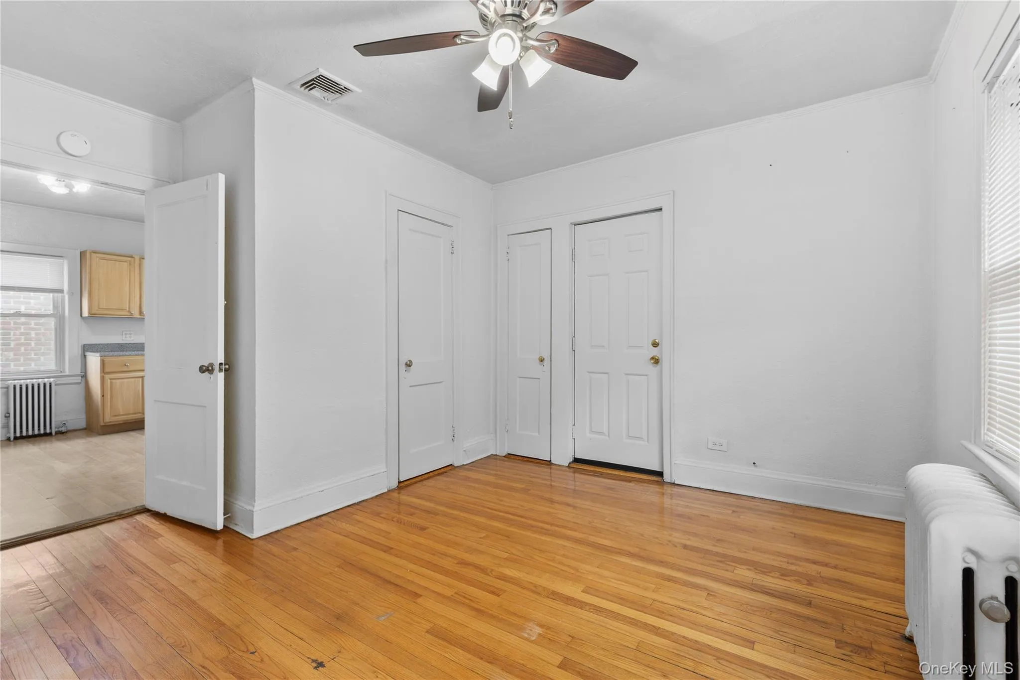 Unfurnished bedroom featuring radiator heating unit, light wood-style flooring, and a ceiling fan Unfurnished bedroom featuring radiator heating unit, light wood-style flooring, and a ceiling fan