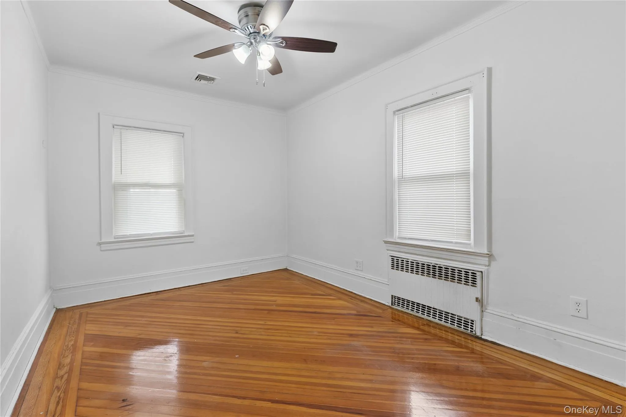 Unfurnished room featuring radiator, hardwood / wood-style floors, crown molding, healthy amount of natural light, and ceiling fan Unfurnished room featuring radiator, hardwood / wood-style floors, crown molding, healthy amount of natural light, and ceiling fan