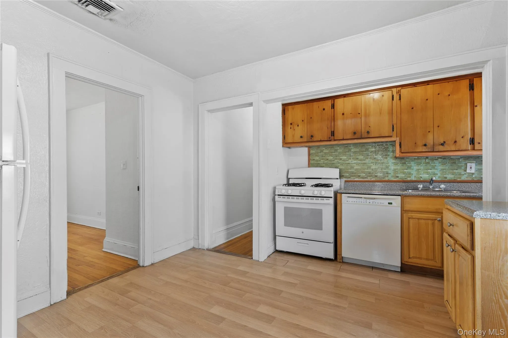 Kitchen featuring decorative backsplash, white appliances, light wood finished floors, and brown cabinetry Kitchen featuring decorative backsplash, white appliances, light wood finished floors, and brown cabinetry
