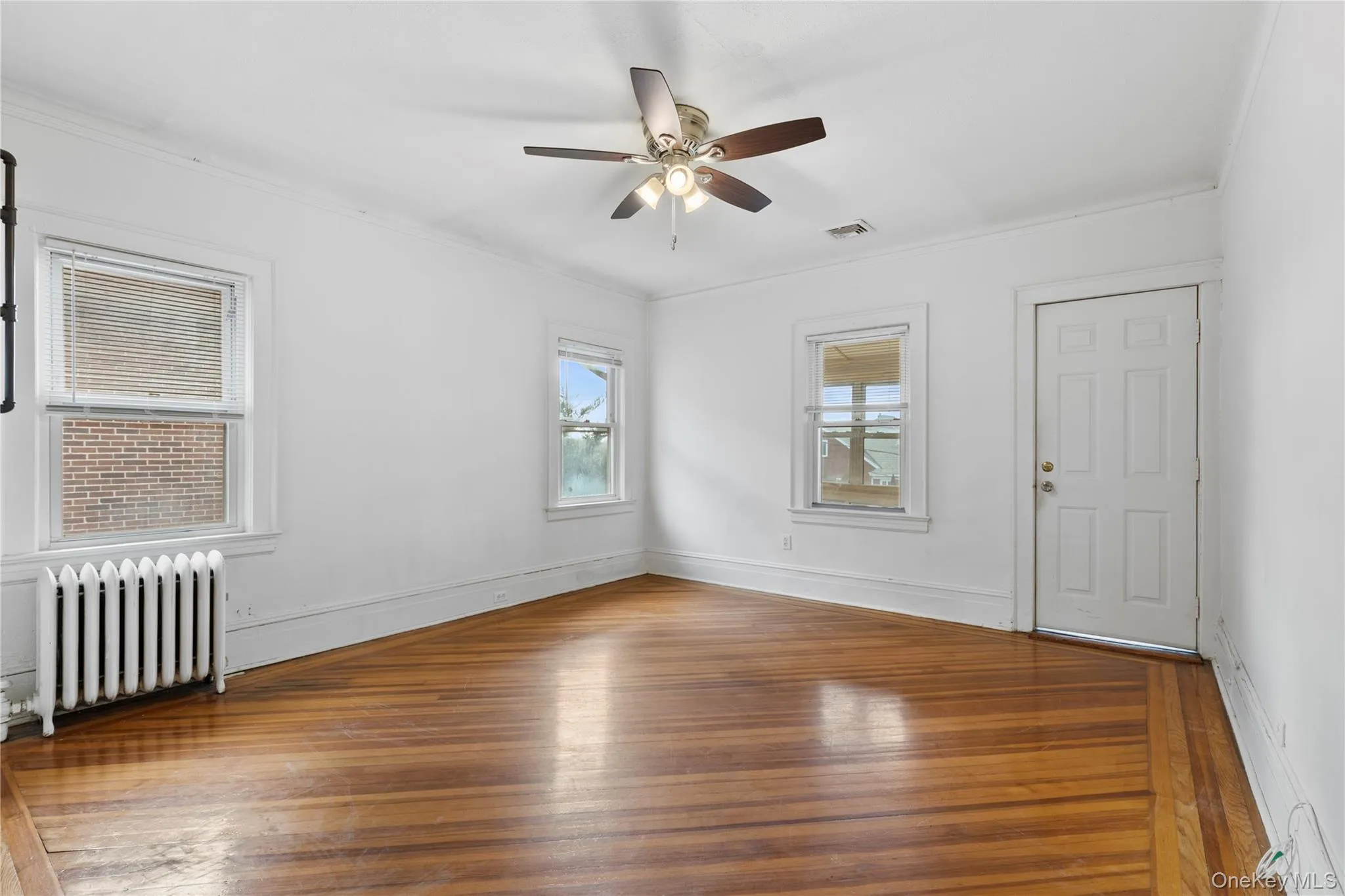 Empty room featuring radiator, hardwood / wood-style floors, crown molding, and ceiling fan Empty room featuring radiator, hardwood / wood-style floors, crown molding, and ceiling fan