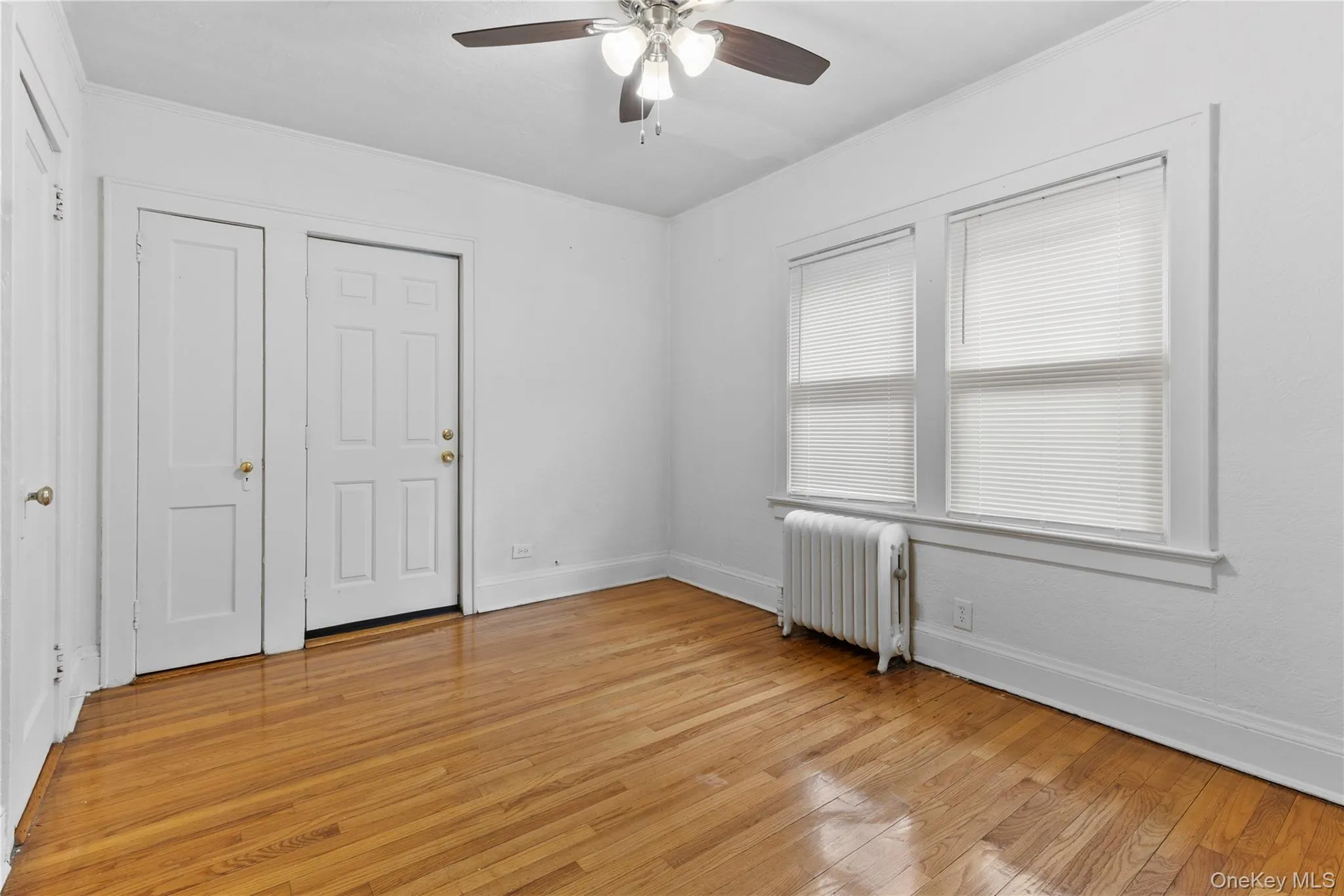 Unfurnished bedroom featuring radiator, light wood-style flooring, and ceiling fan Unfurnished bedroom featuring radiator, light wood-style flooring, and ceiling fan