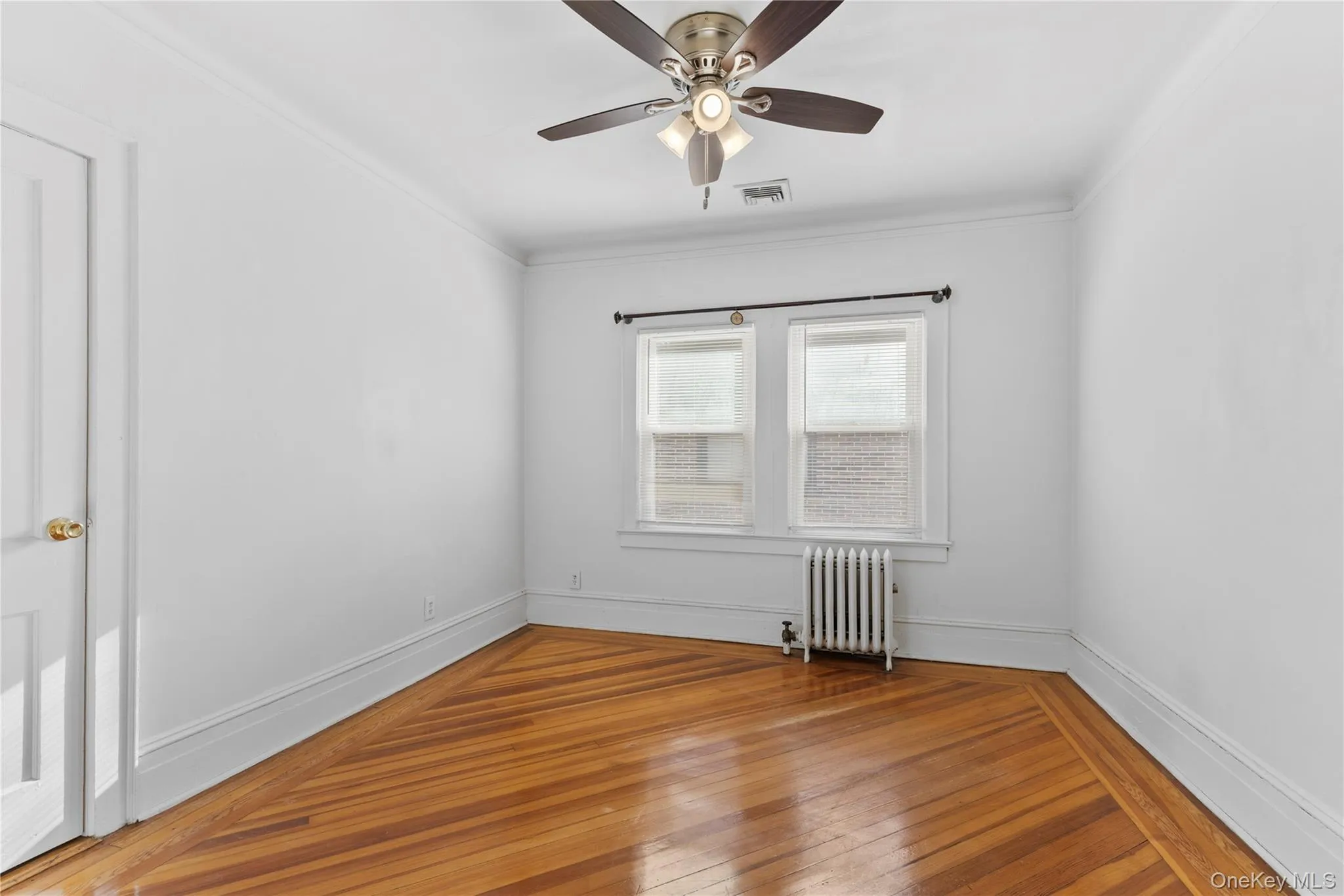 Empty room featuring radiator, crown molding, hardwood / wood-style flooring, and ceiling fan Empty room featuring radiator, crown molding, hardwood / wood-style flooring, and ceiling fan