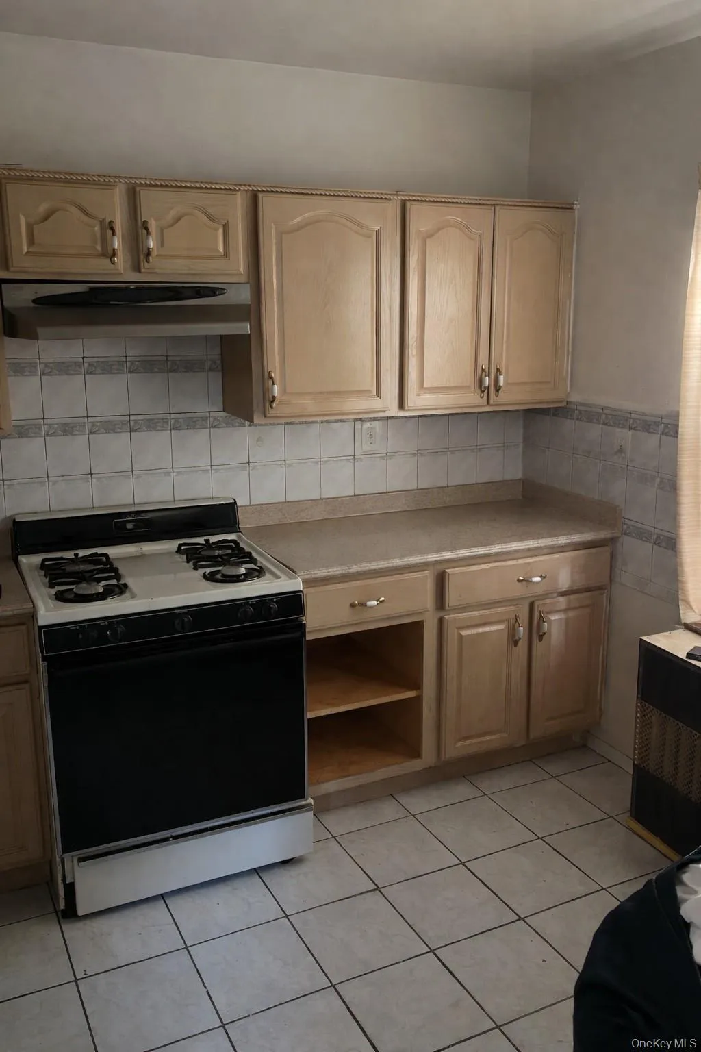 Kitchen with gas stove, light countertops, light tile patterned flooring, under cabinet range hood, and tile walls Kitchen with gas stove, light countertops, light tile patterned flooring, under cabinet range hood, and tile walls