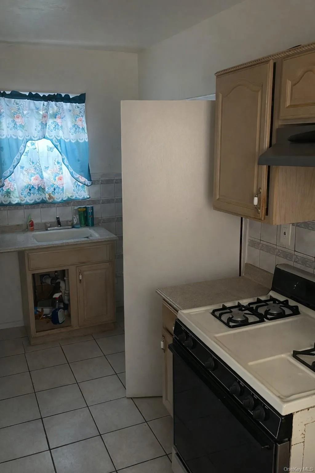 Kitchen with white range with gas cooktop, light countertops, under cabinet range hood, light tile patterned floors, and light brown cabinetry Kitchen with white range with gas cooktop, light countertops, under cabinet range hood, light tile patterned floors, and light brown cabinetry