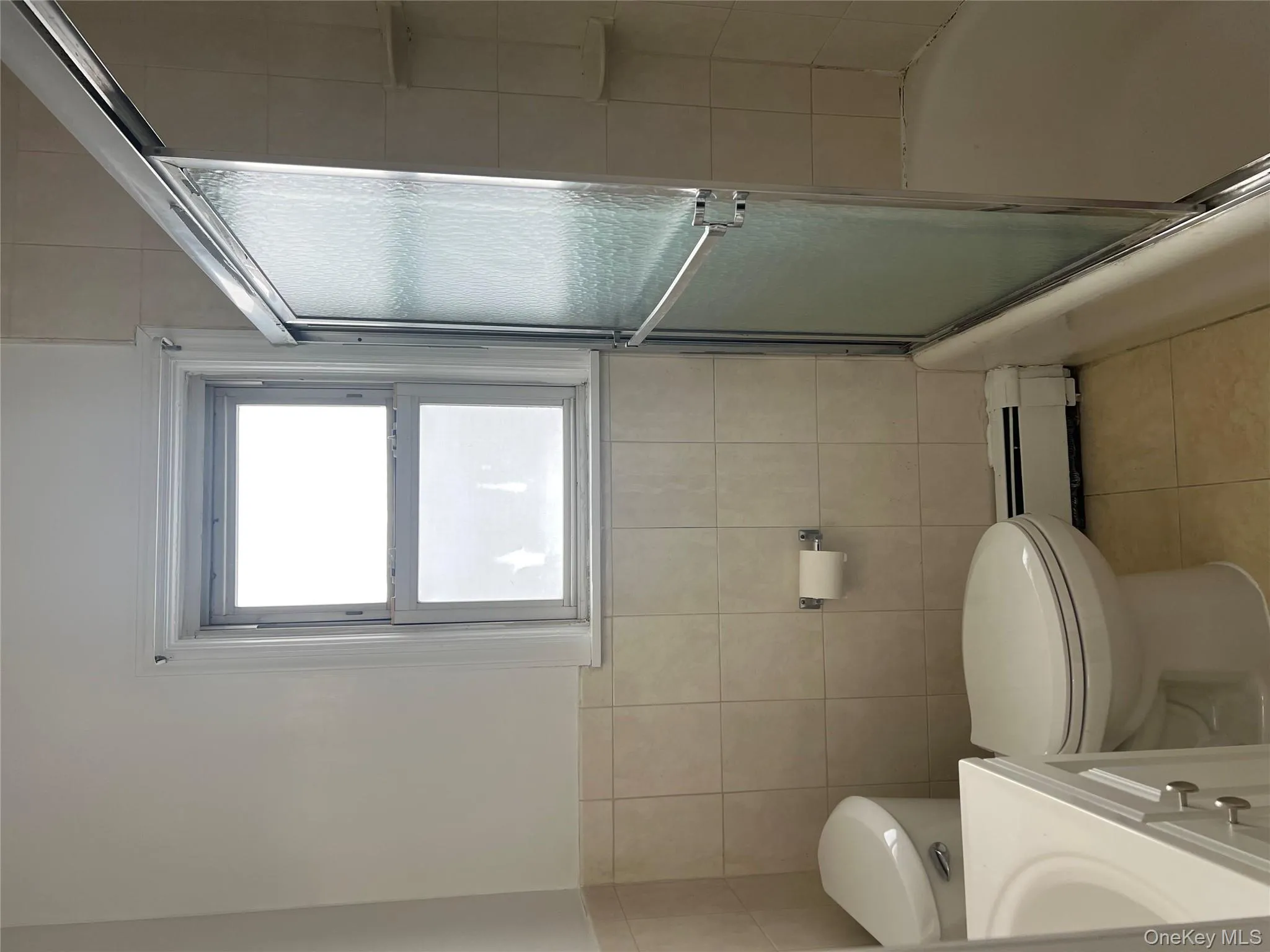 Bathroom featuring vanity, light tile patterned floors, baseboard heating, combined bath / shower with glass door, and tile walls Bathroom featuring vanity, light tile patterned floors, baseboard heating, combined bath / shower with glass door, and tile walls