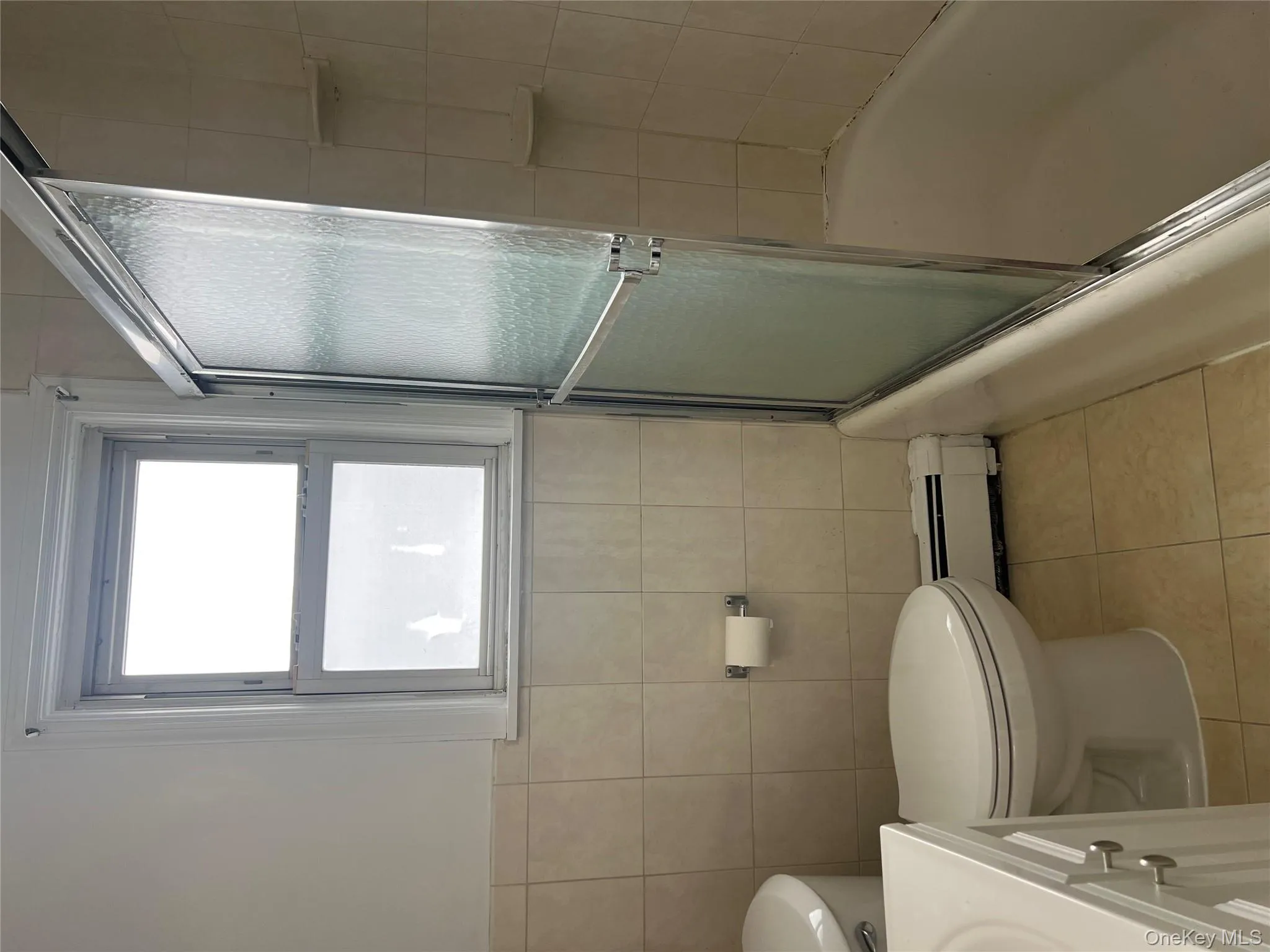 Bathroom with vanity, light tile patterned floors, a baseboard heating unit, enclosed tub / shower combo, and tile walls Bathroom with vanity, light tile patterned floors, a baseboard heating unit, enclosed tub / shower combo, and tile walls