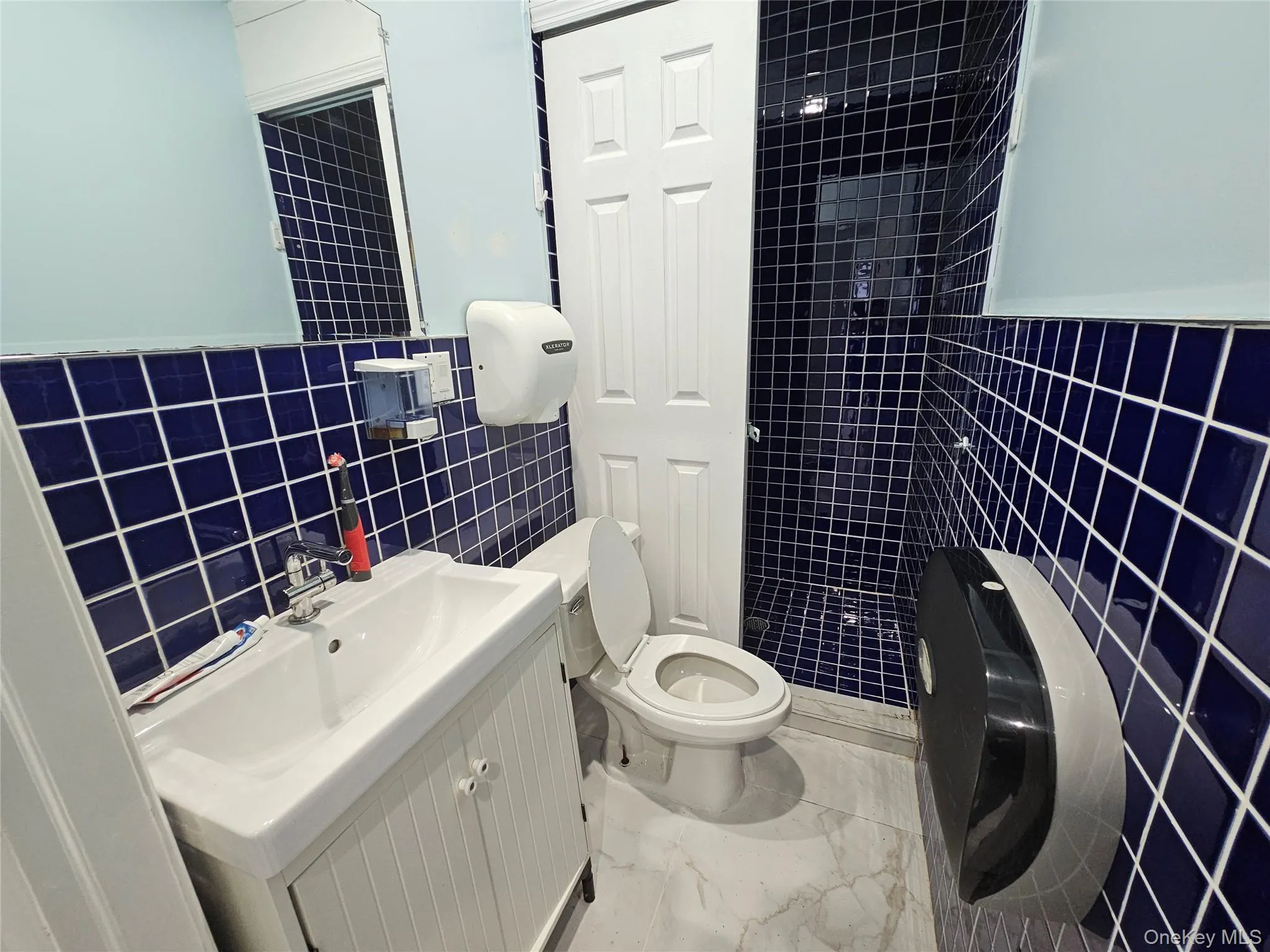 Full bathroom with tile walls, vanity, a wainscoted wall, light marble finish floors, and washer / dryer Full bathroom with tile walls, vanity, a wainscoted wall, light marble finish floors, and washer / dryer
