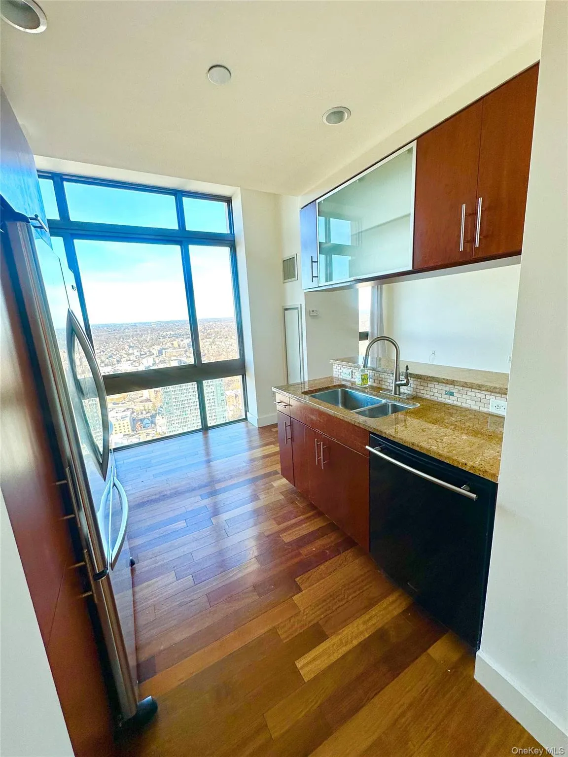 Kitchen with light stone counters, expansive windows, freestanding refrigerator, dishwasher, and dark wood-style flooring Kitchen with light stone counters, expansive windows, freestanding refrigerator, dishwasher, and dark wood-style flooring