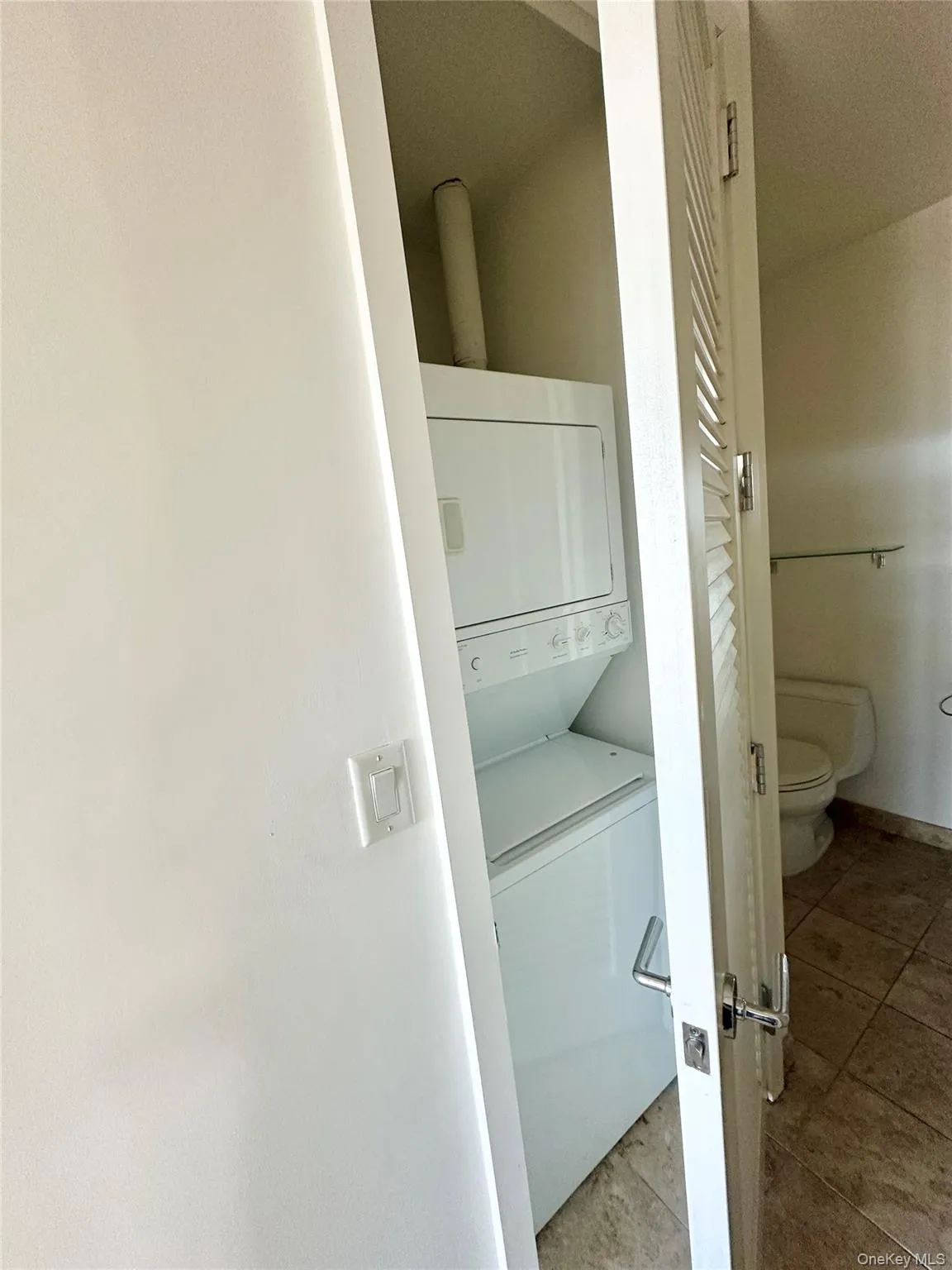 Laundry area with stacked washing machine and dryer and light tile patterned floors Laundry area with stacked washing machine and dryer and light tile patterned floors