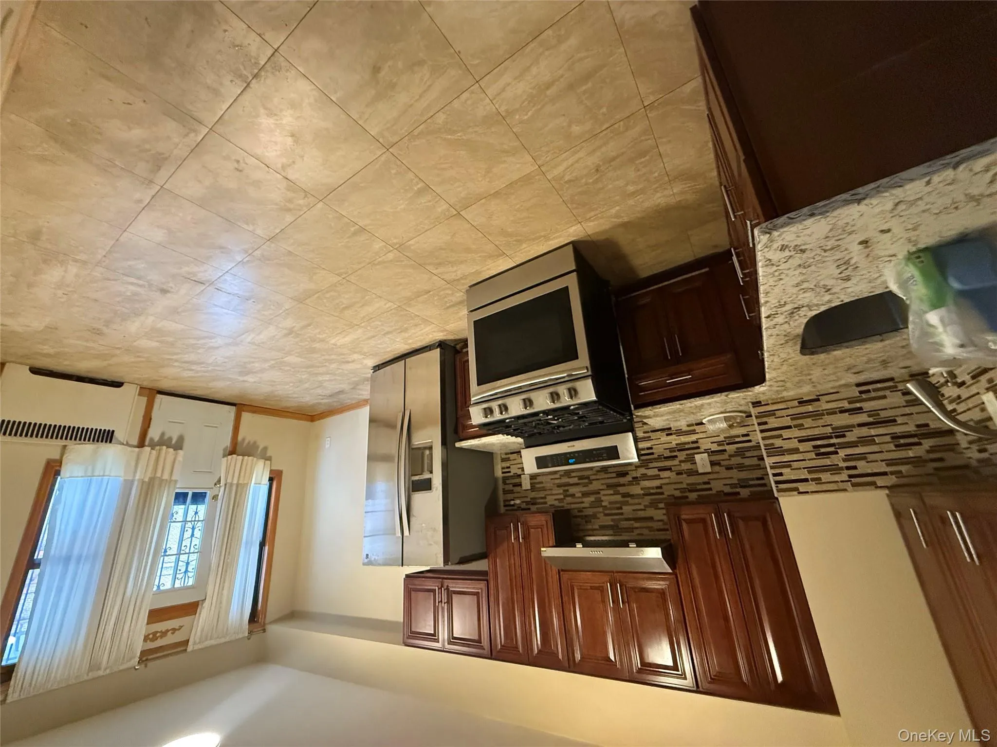 Kitchen featuring appliances with stainless steel finishes, light stone countertops, dark brown cabinetry, radiator, and tasteful backsplash Kitchen featuring appliances with stainless steel finishes, light stone countertops, dark brown cabinetry, radiator, and tasteful backsplash