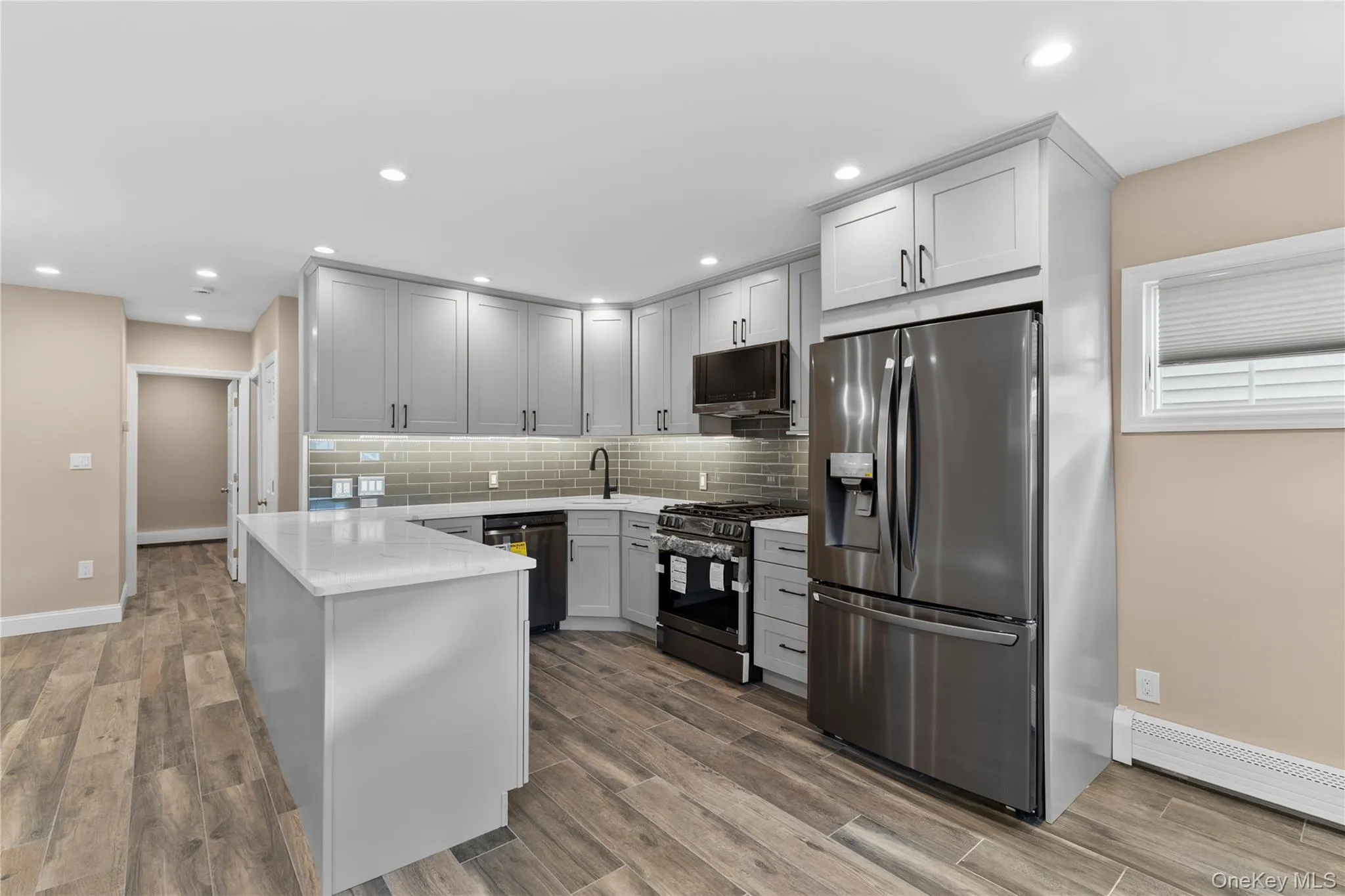 Kitchen with appliances with stainless steel finishes, a peninsula, light stone countertops, light wood-type flooring, and recessed lighting Kitchen with appliances with stainless steel finishes, a peninsula, light stone countertops, light wood-type flooring, and recessed lighting