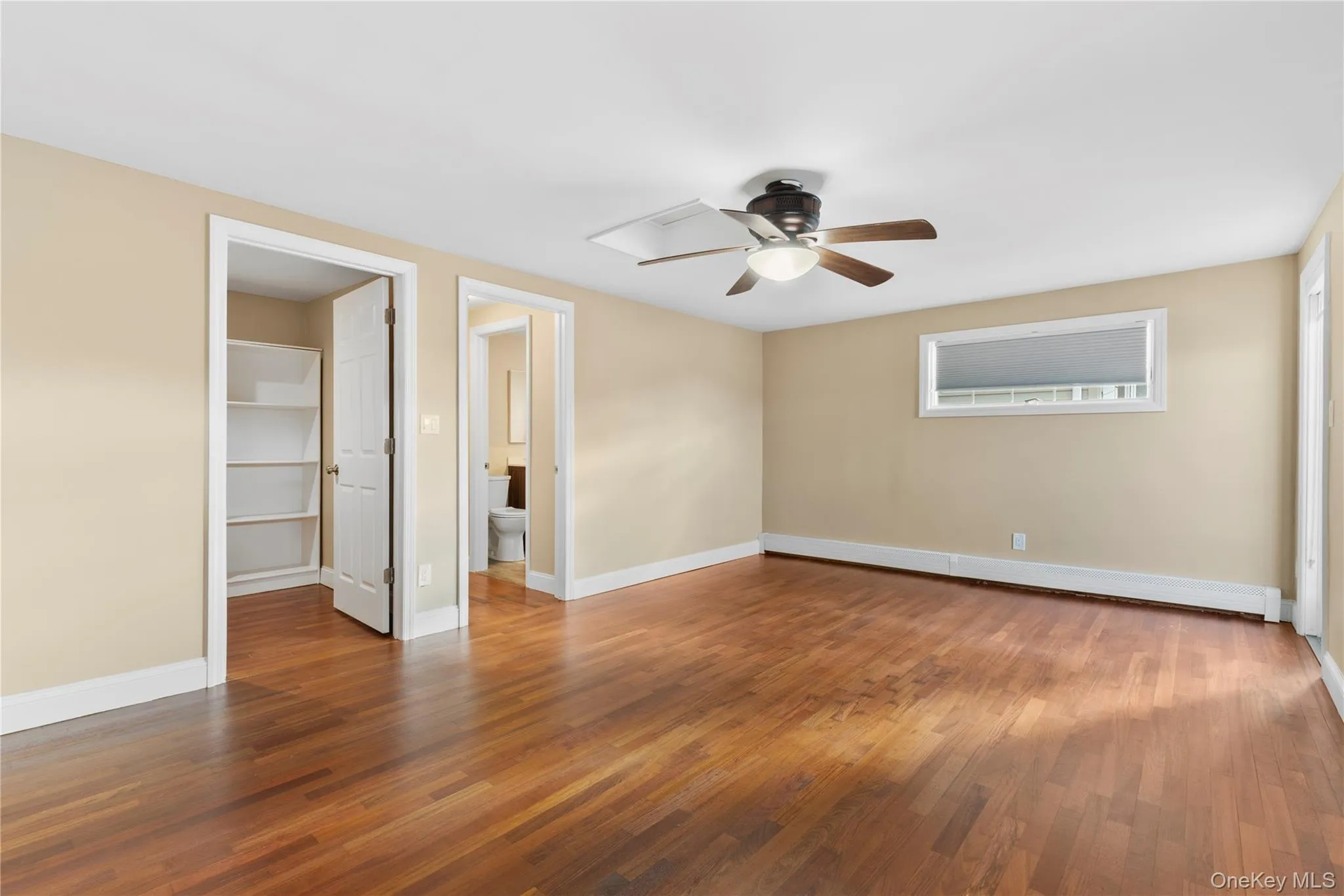Unfurnished bedroom with a walk in closet, hardwood / wood-style floors, ceiling fan, a baseboard heating unit, and attic access Unfurnished bedroom with a walk in closet, hardwood / wood-style floors, ceiling fan, a baseboard heating unit, and attic access