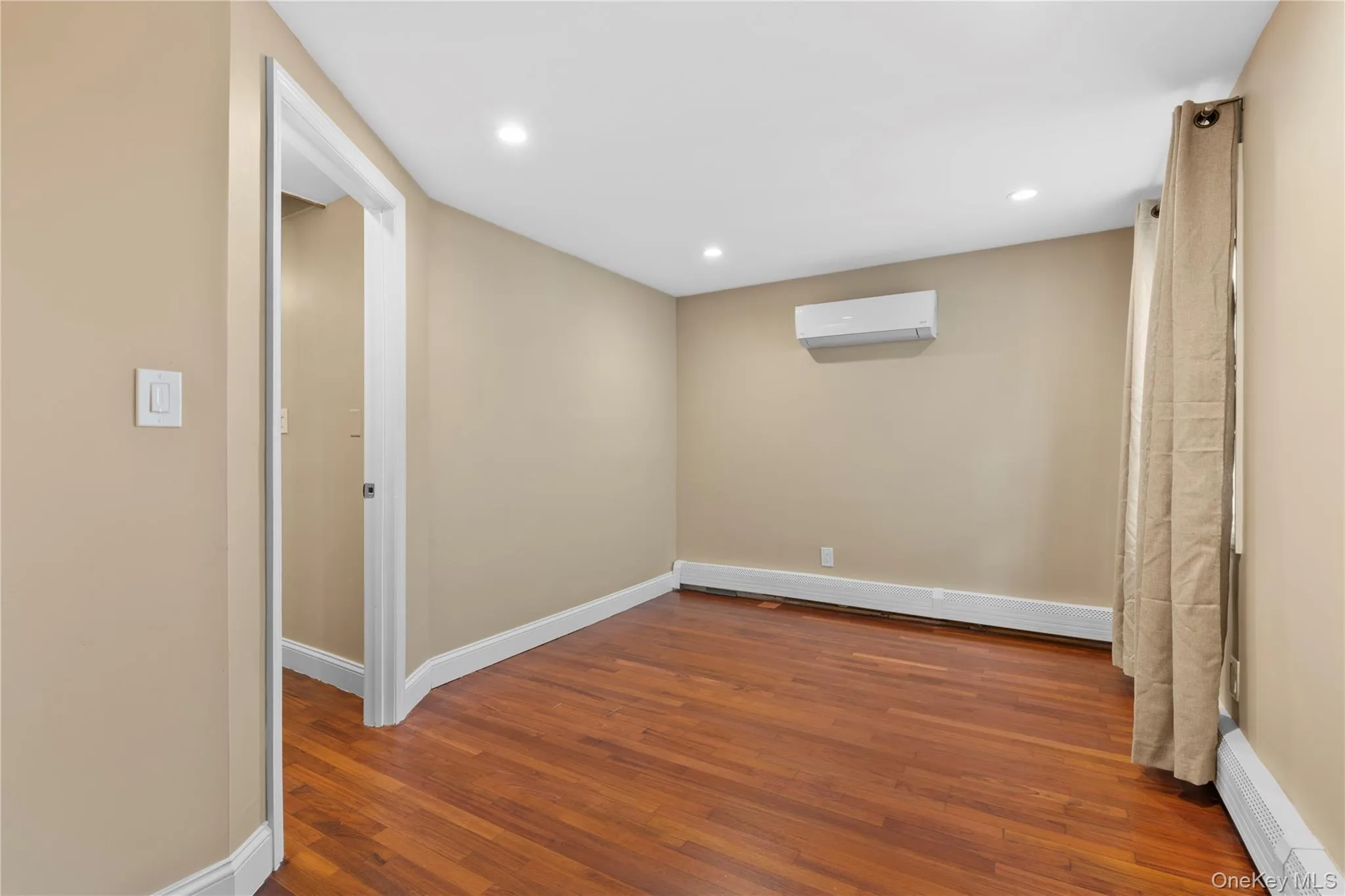 Below grade area with a baseboard heating unit, wood-type flooring, recessed lighting, and a wall mounted air conditioner Below grade area with a baseboard heating unit, wood-type flooring, recessed lighting, and a wall mounted air conditioner