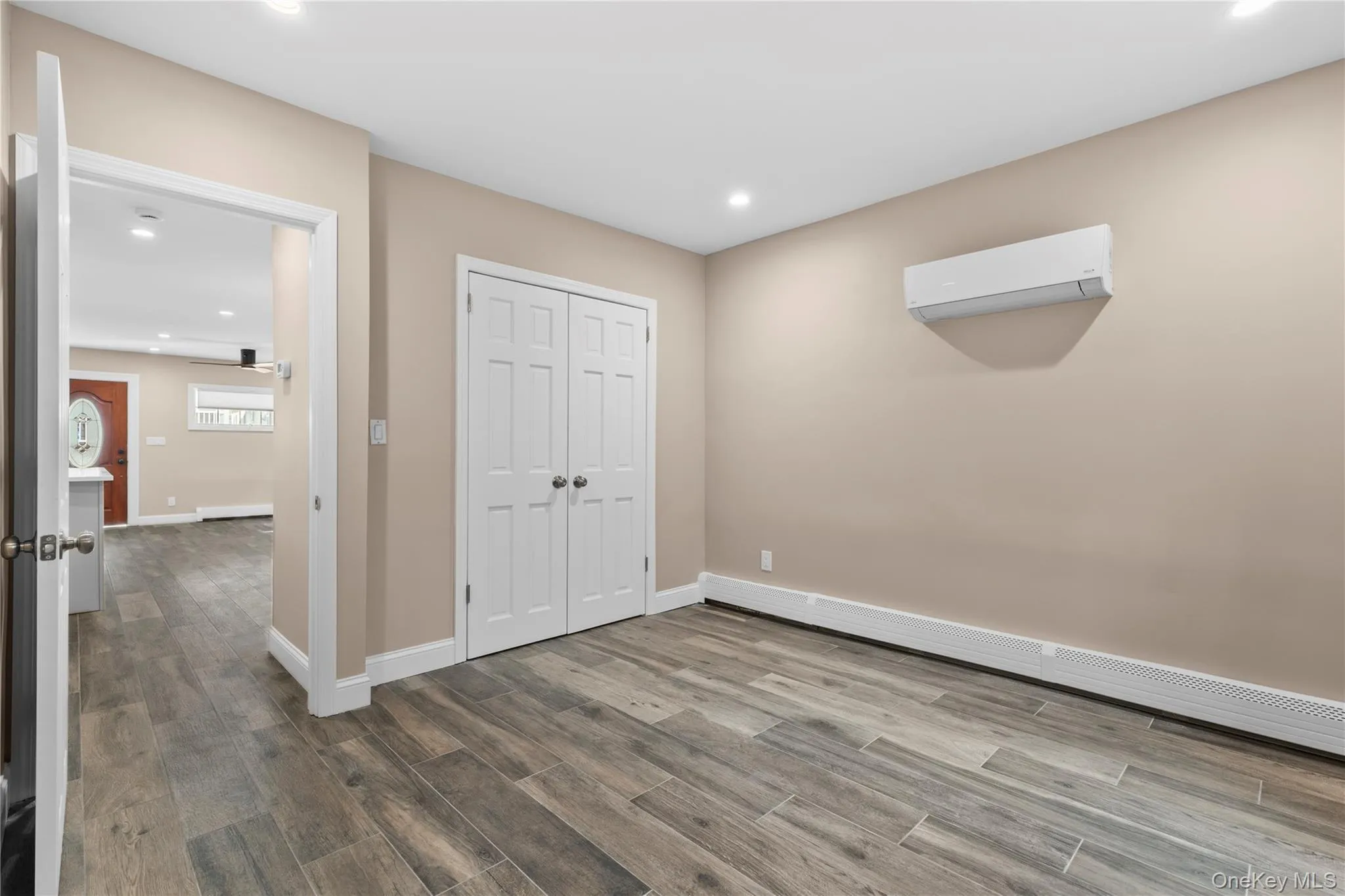 Unfurnished bedroom with recessed lighting, wood finished floors, a baseboard radiator, a closet, and a wall mounted air conditioner Unfurnished bedroom with recessed lighting, wood finished floors, a baseboard radiator, a closet, and a wall mounted air conditioner