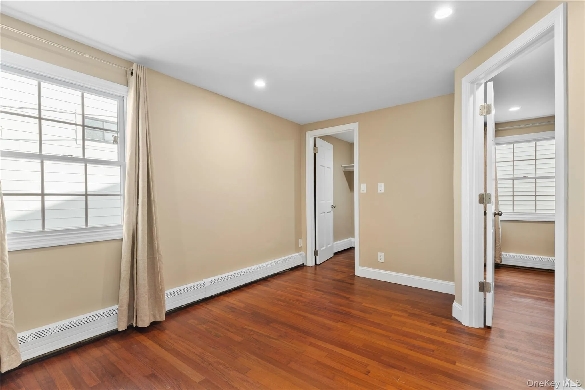 Unfurnished bedroom with a baseboard heating unit, dark wood finished floors, a walk in closet, and recessed lighting Unfurnished bedroom with a baseboard heating unit, dark wood finished floors, a walk in closet, and recessed lighting