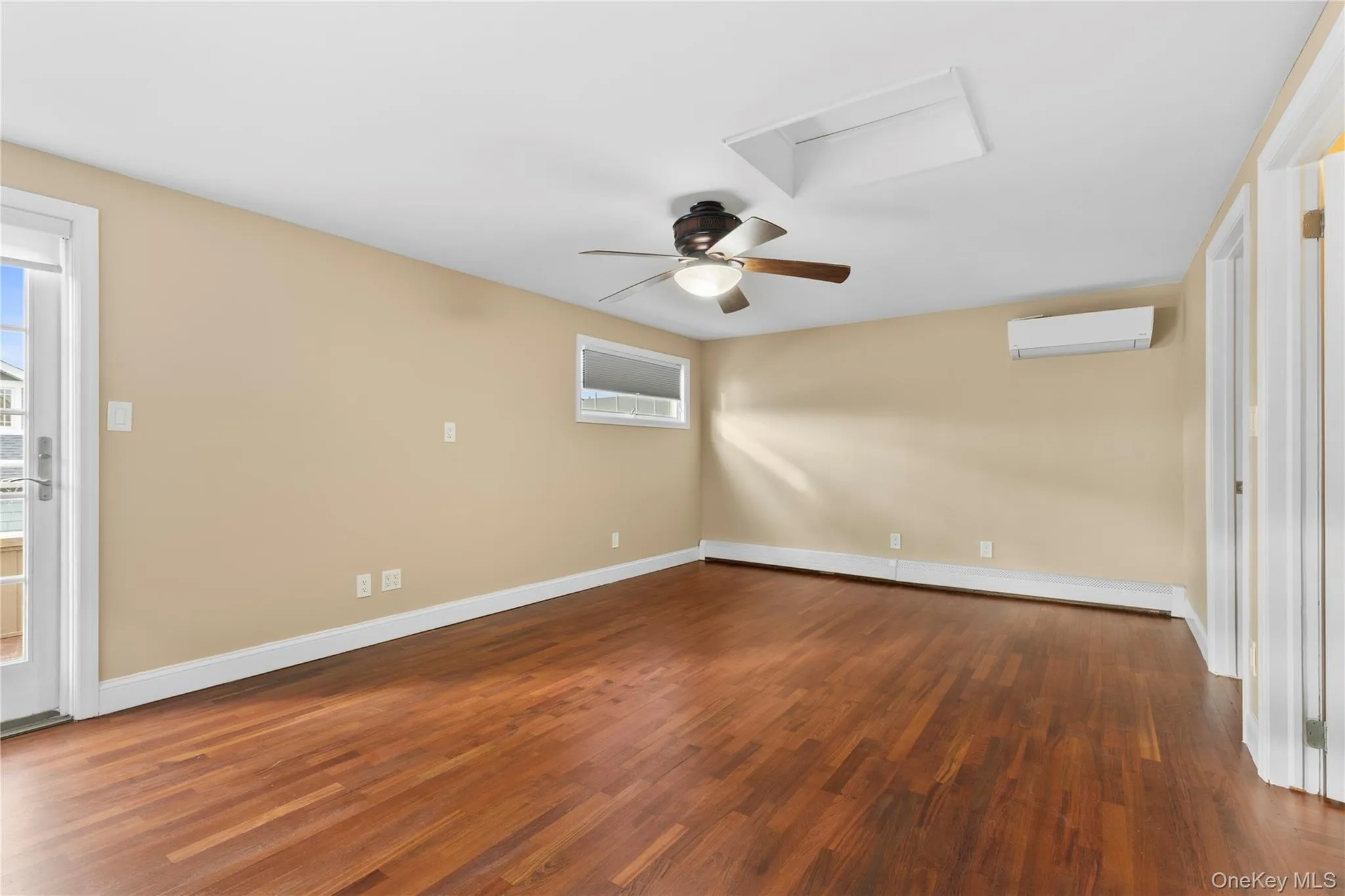 Unfurnished room featuring a ceiling fan, dark wood-style flooring, a wall unit AC, attic access, and a baseboard radiator Unfurnished room featuring a ceiling fan, dark wood-style flooring, a wall unit AC, attic access, and a baseboard radiator