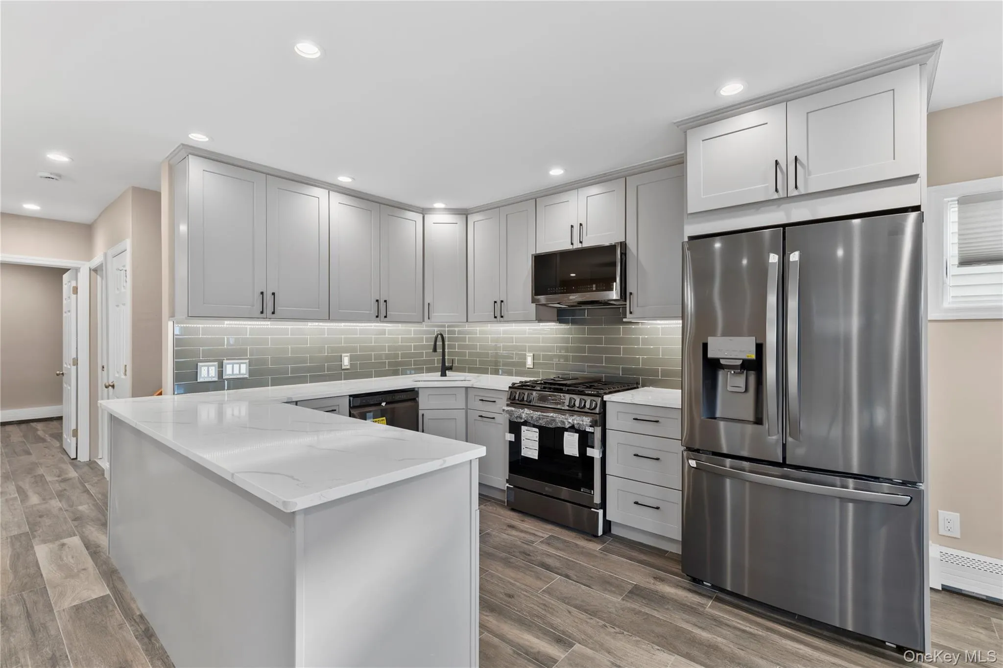 Kitchen with stainless steel appliances, a peninsula, light stone countertops, wood finish floors, and recessed lighting Kitchen with stainless steel appliances, a peninsula, light stone countertops, wood finish floors, and recessed lighting