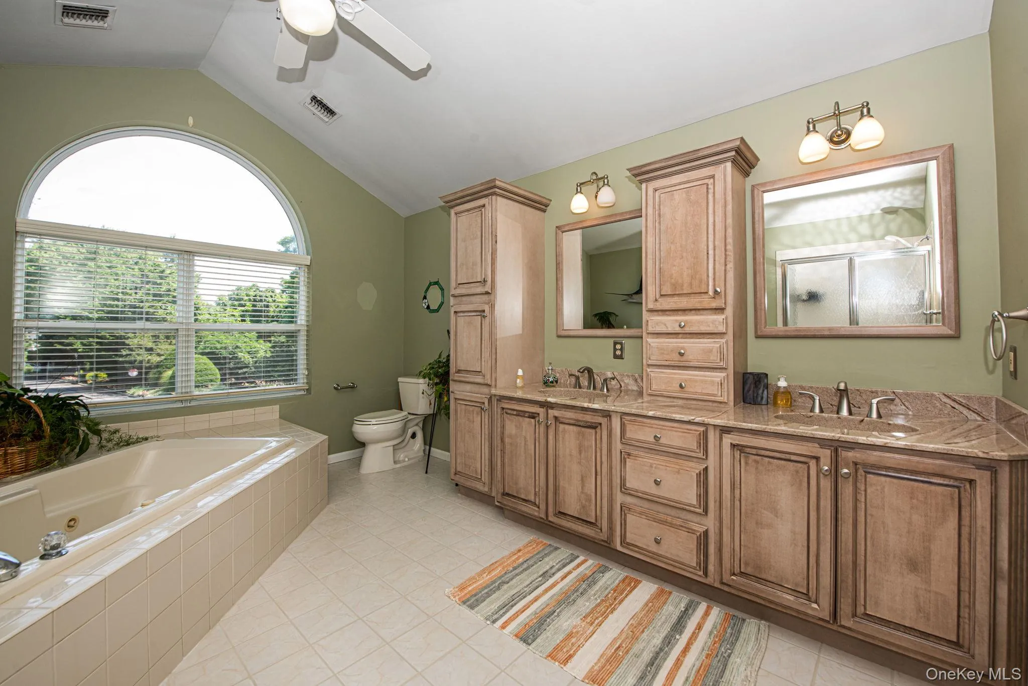 Full bathroom with double vanity, light tile patterned flooring, lofted ceiling, a whirlpool tub, and ceiling fan Full bathroom with double vanity, light tile patterned flooring, lofted ceiling, a whirlpool tub, and ceiling fan