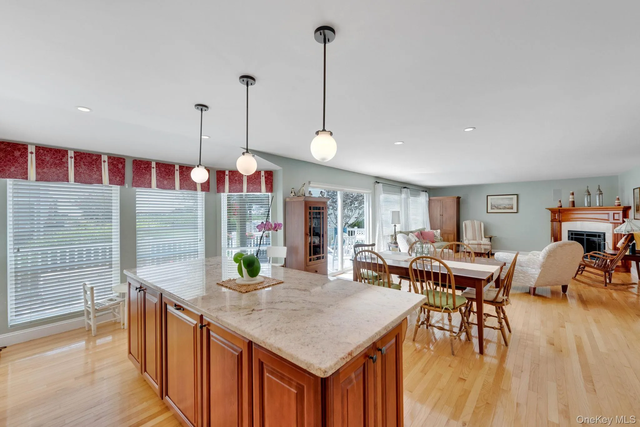 Kitchen featuring brown cabinetry, hanging light fixtures, a fireplace, light stone countertops, and light wood-style flooring Kitchen featuring brown cabinetry, hanging light fixtures, a fireplace, light stone countertops, and light wood-style flooring