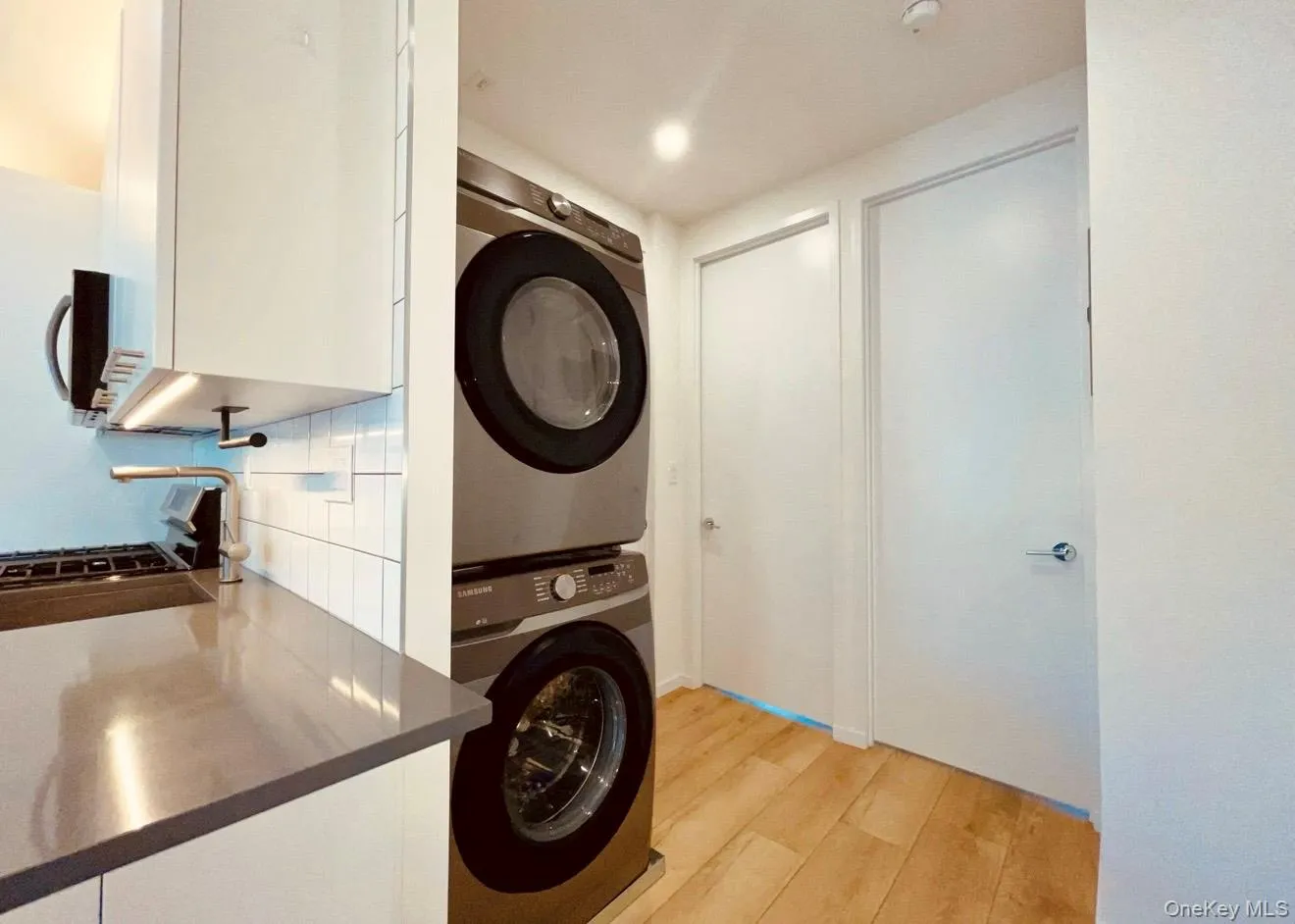 Washroom with stacked washing machine and dryer and light wood-type flooring Washroom with stacked washing machine and dryer and light wood-type flooring