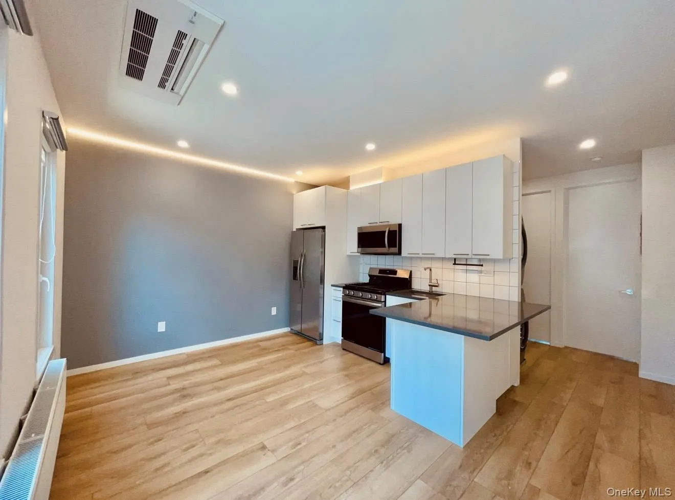 Kitchen featuring white cabinets, stainless steel appliances, decorative backsplash, cooling unit, and light wood-style floors Kitchen featuring white cabinets, stainless steel appliances, decorative backsplash, cooling unit, and light wood-style floors