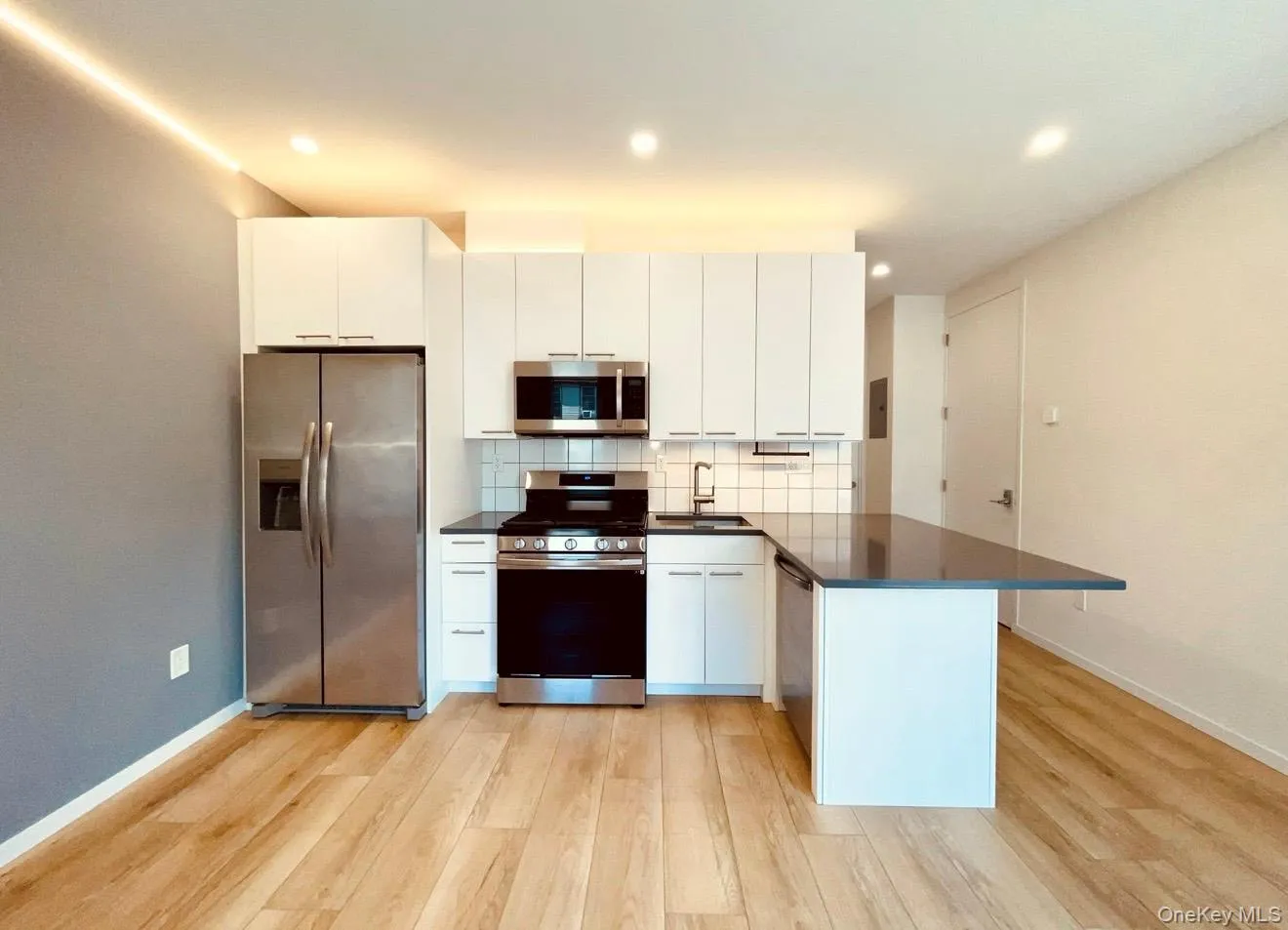 Kitchen featuring appliances with stainless steel finishes, white cabinetry, backsplash, a peninsula, and light wood finished floors Kitchen featuring appliances with stainless steel finishes, white cabinetry, backsplash, a peninsula, and light wood finished floors