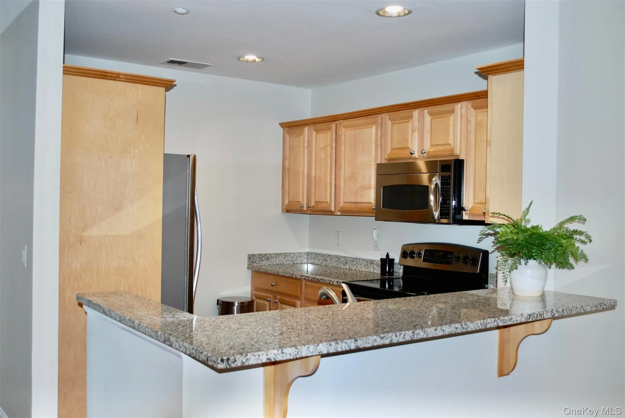 Kitchen featuring stainless steel appliances, light stone counters, light brown cabinetry, a peninsula, and recessed lighting Kitchen featuring stainless steel appliances, light stone counters, light brown cabinetry, a peninsula, and recessed lighting