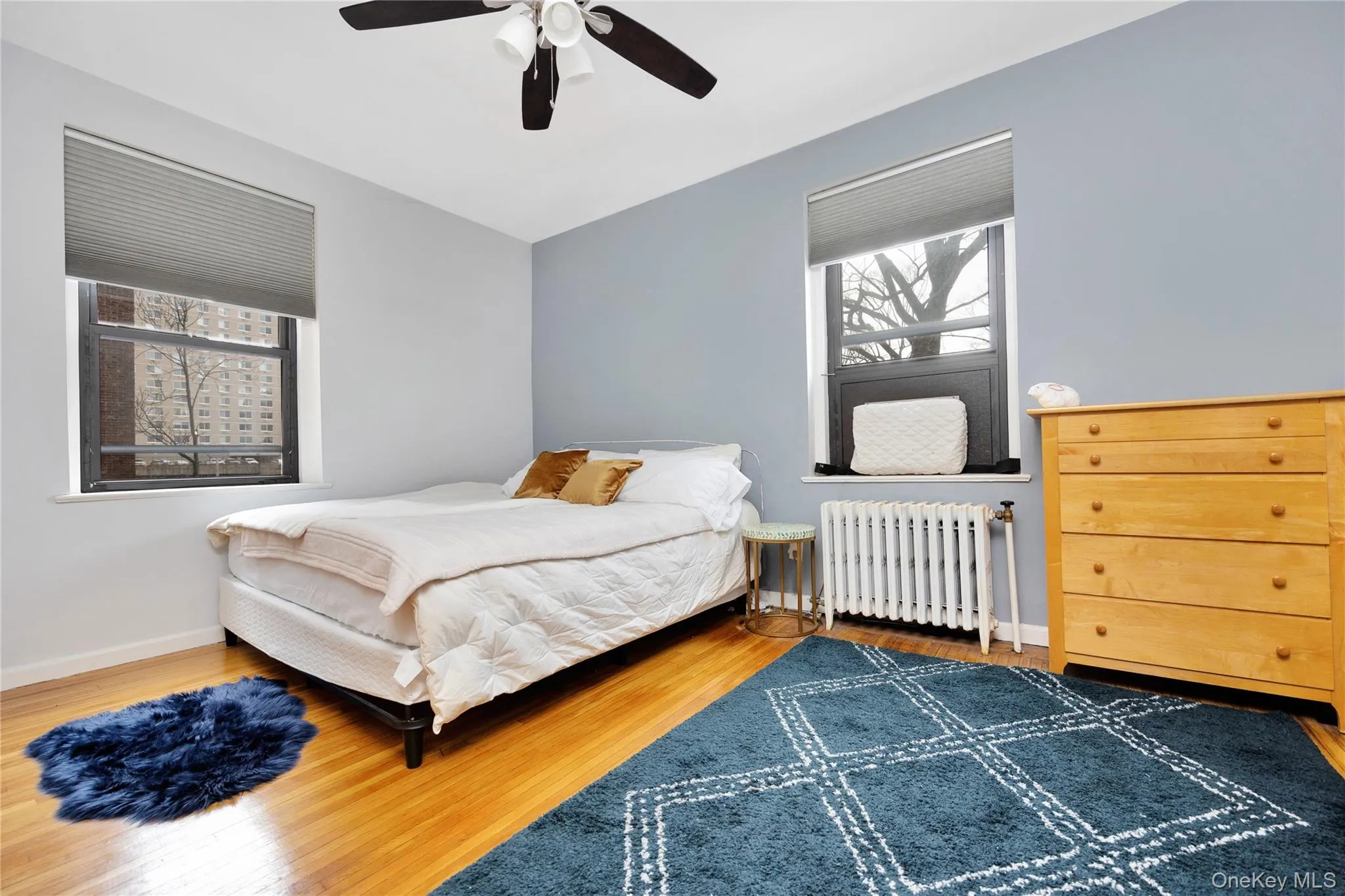 Bedroom featuring radiator heating unit, wood finished floors, and ceiling fan Bedroom featuring radiator heating unit, wood finished floors, and ceiling fan
